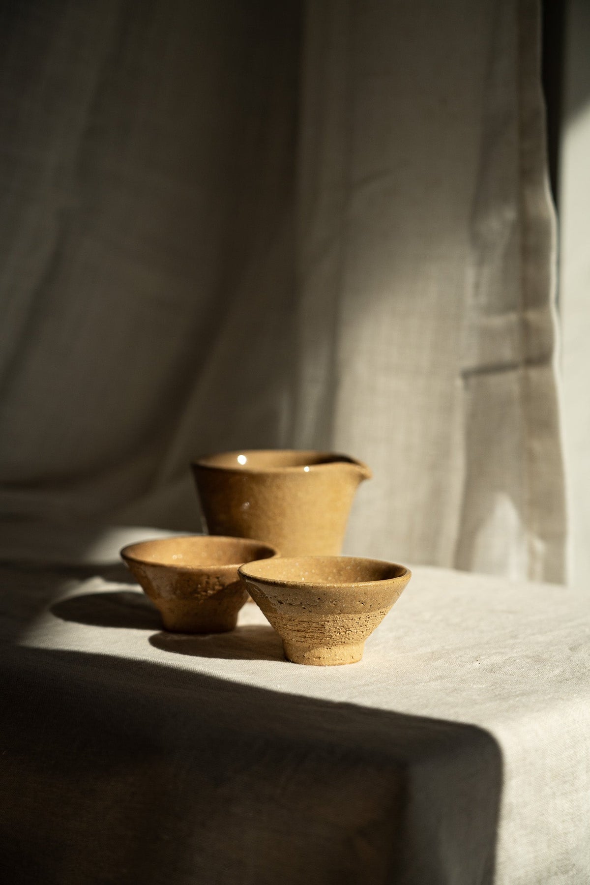 Handmade Stoneware Fair Teacup set with a warm ochre glaze, fine speckles, and a handleless pitcher shape.