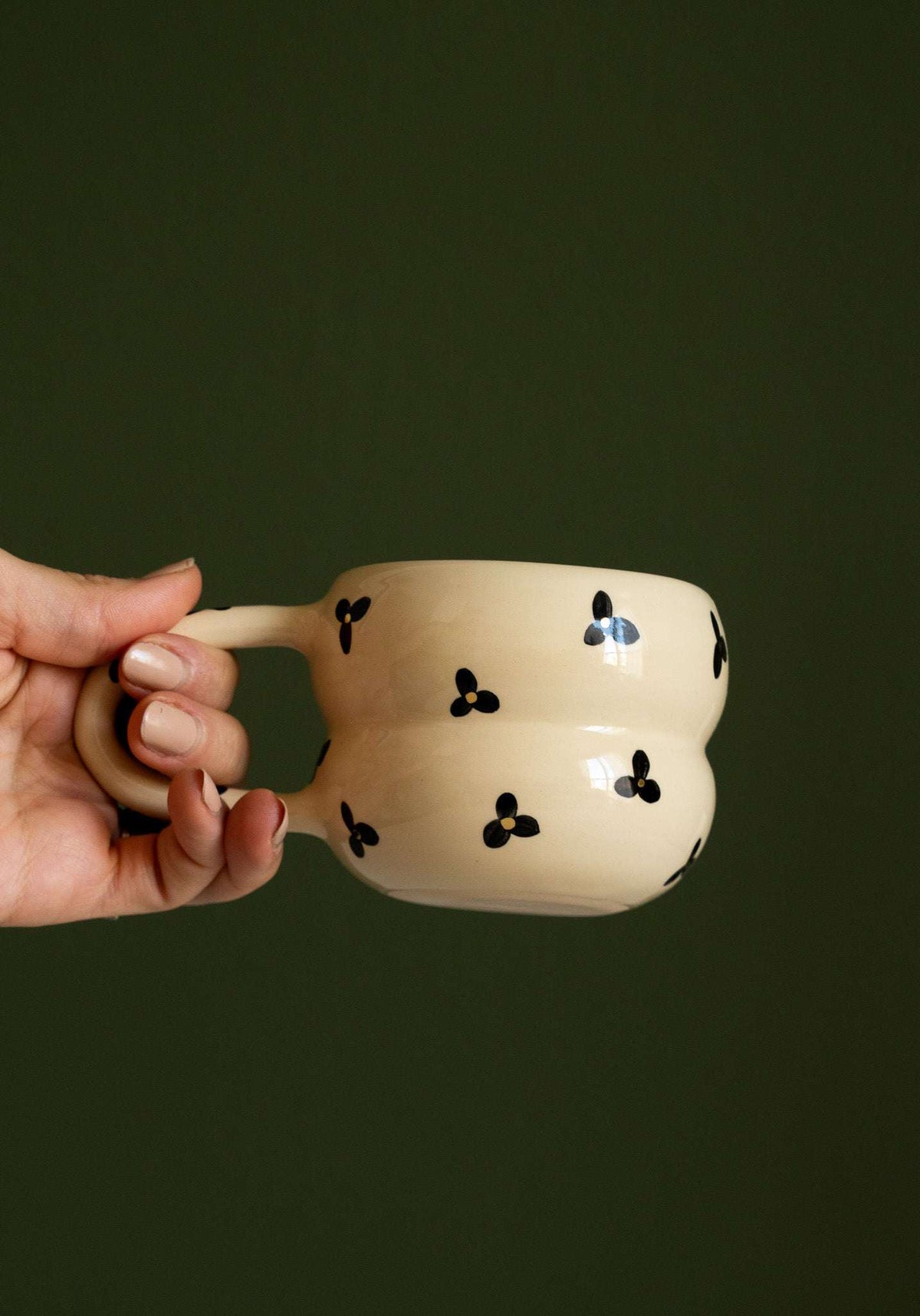 Bubble Mug in cream ceramic with a rounded double-ring shape and black three-petal flowers with golden centers