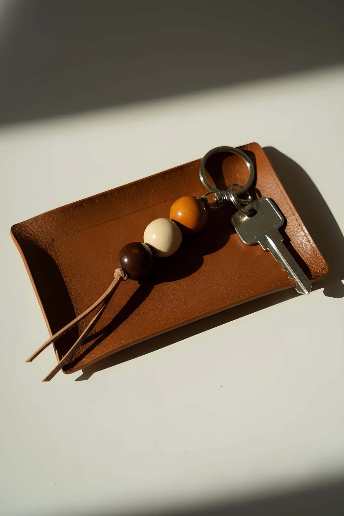 Ceramic Keychain with three glossy brown, cream and amber ceramic beads, dark leather cord, and silver-tone chain and key ring.