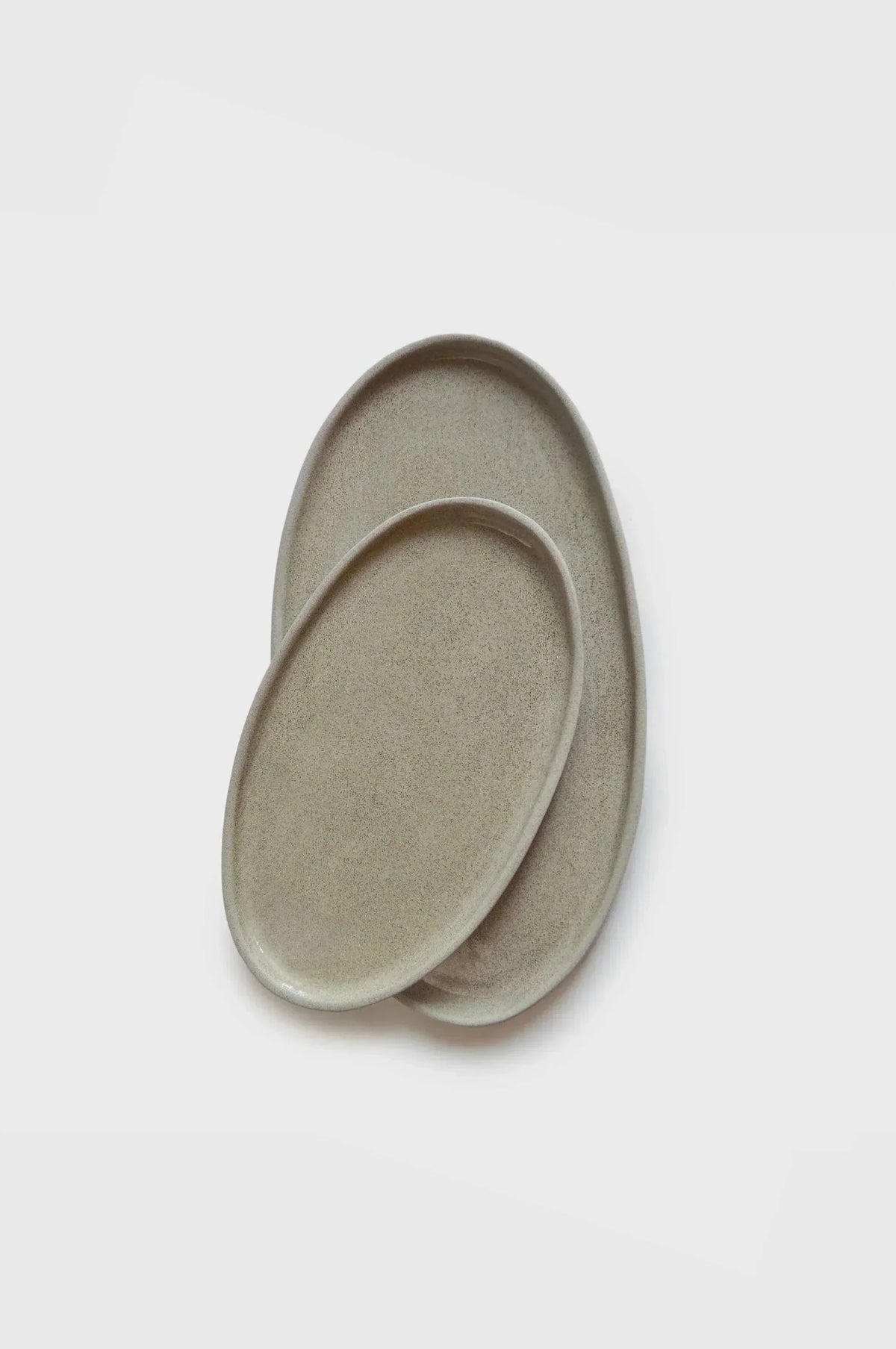 Handmade Stoneware serving platters in muted gray-beige, with elongated oval shapes and subtly textured surfaces.