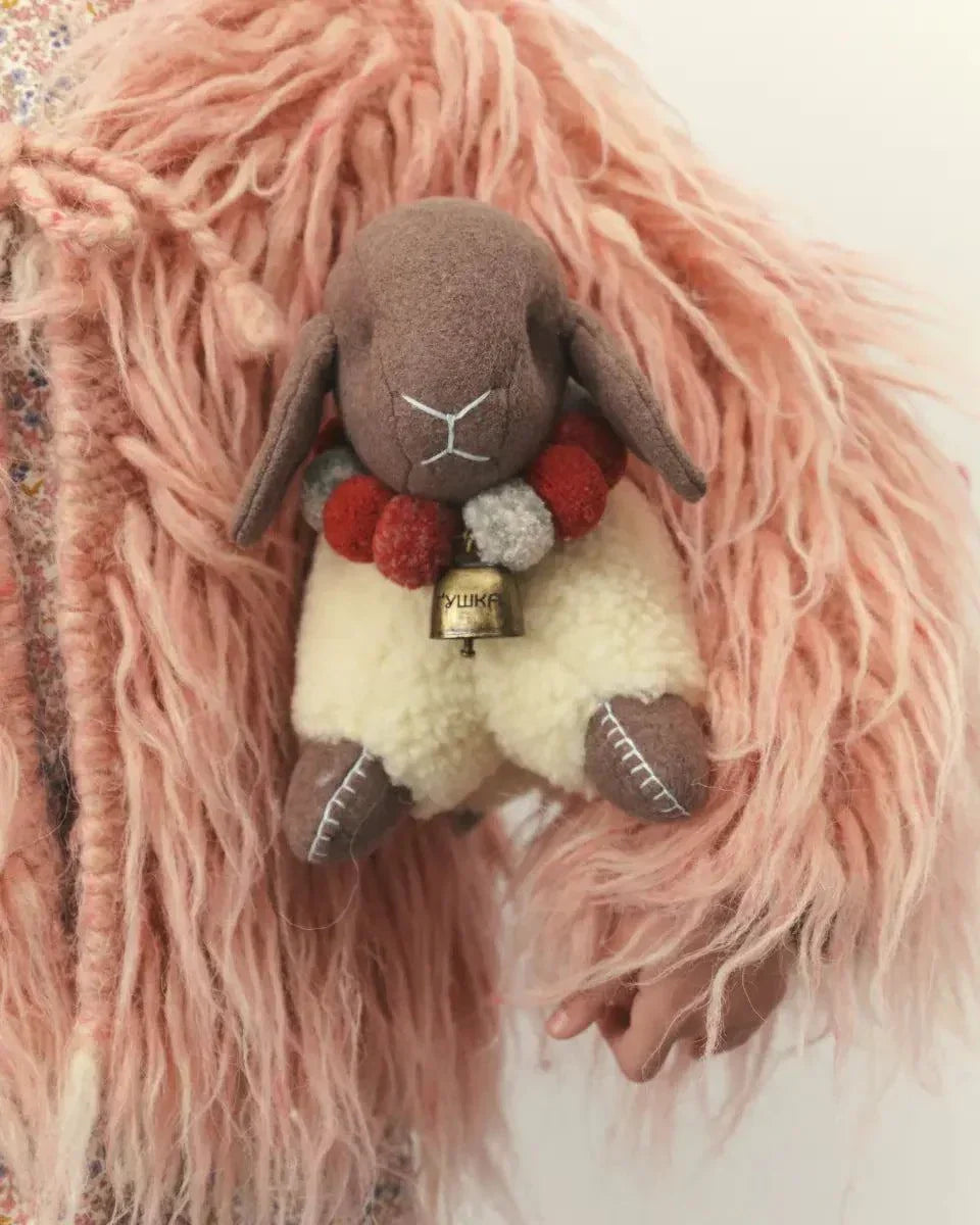 Wool Lamb Toy with a cream fluffy wool body, brown fleece face and legs, red pom-pom collar, and small bell.