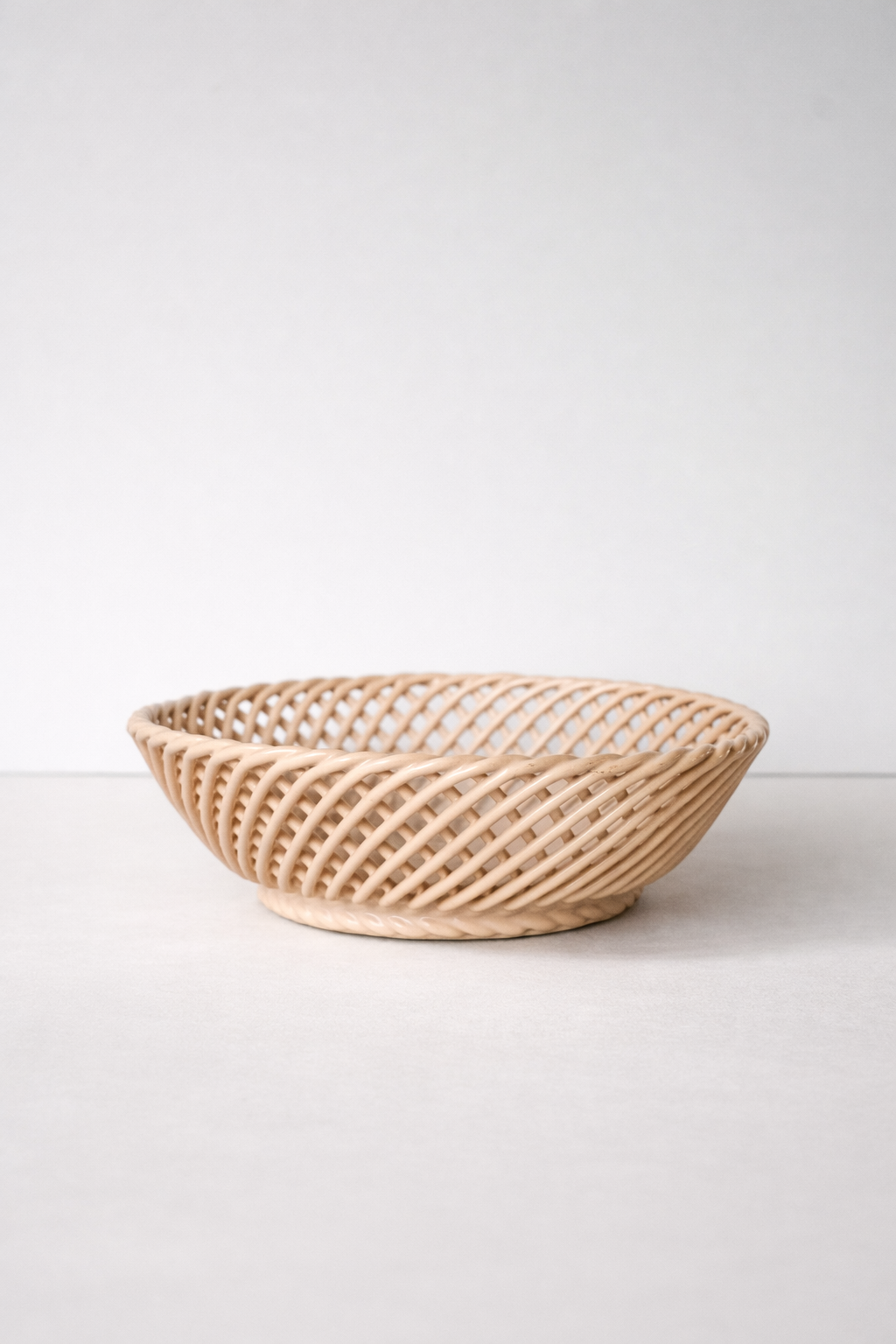 Ceramic Round Hand-Woven Basket in glossy beige porcelain, with an open crisscross weave and shallow rounded shape.