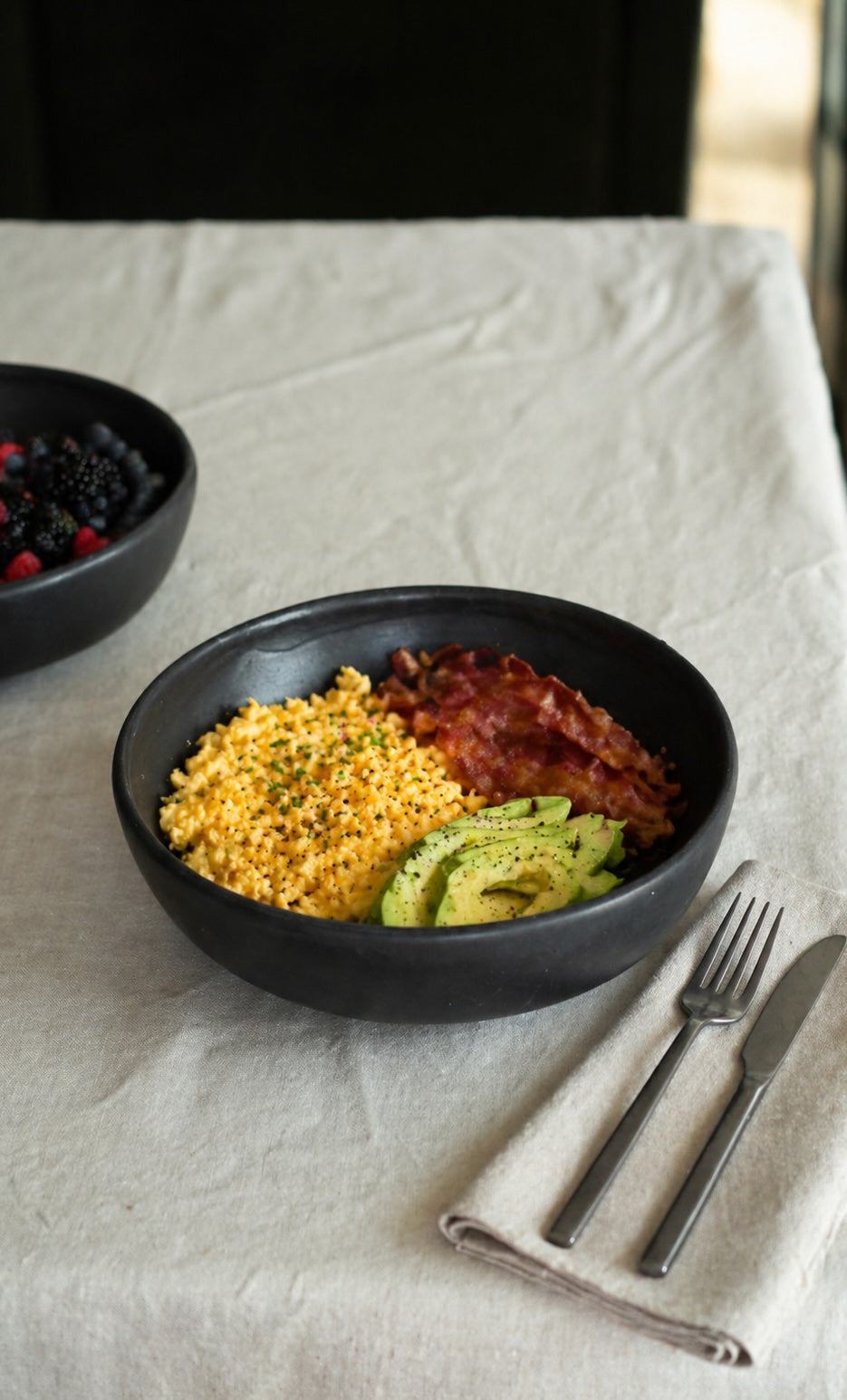Black stoneware pasta bowl with a matte finish, rounded low profile and gently sloped sides, holding a meal
