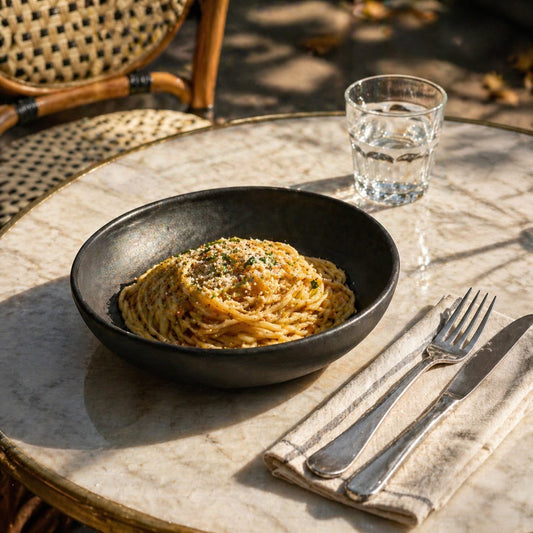 Stoneware pasta bowl in black matte glaze with a broad, low-profile shape and smooth, gently curved rim.