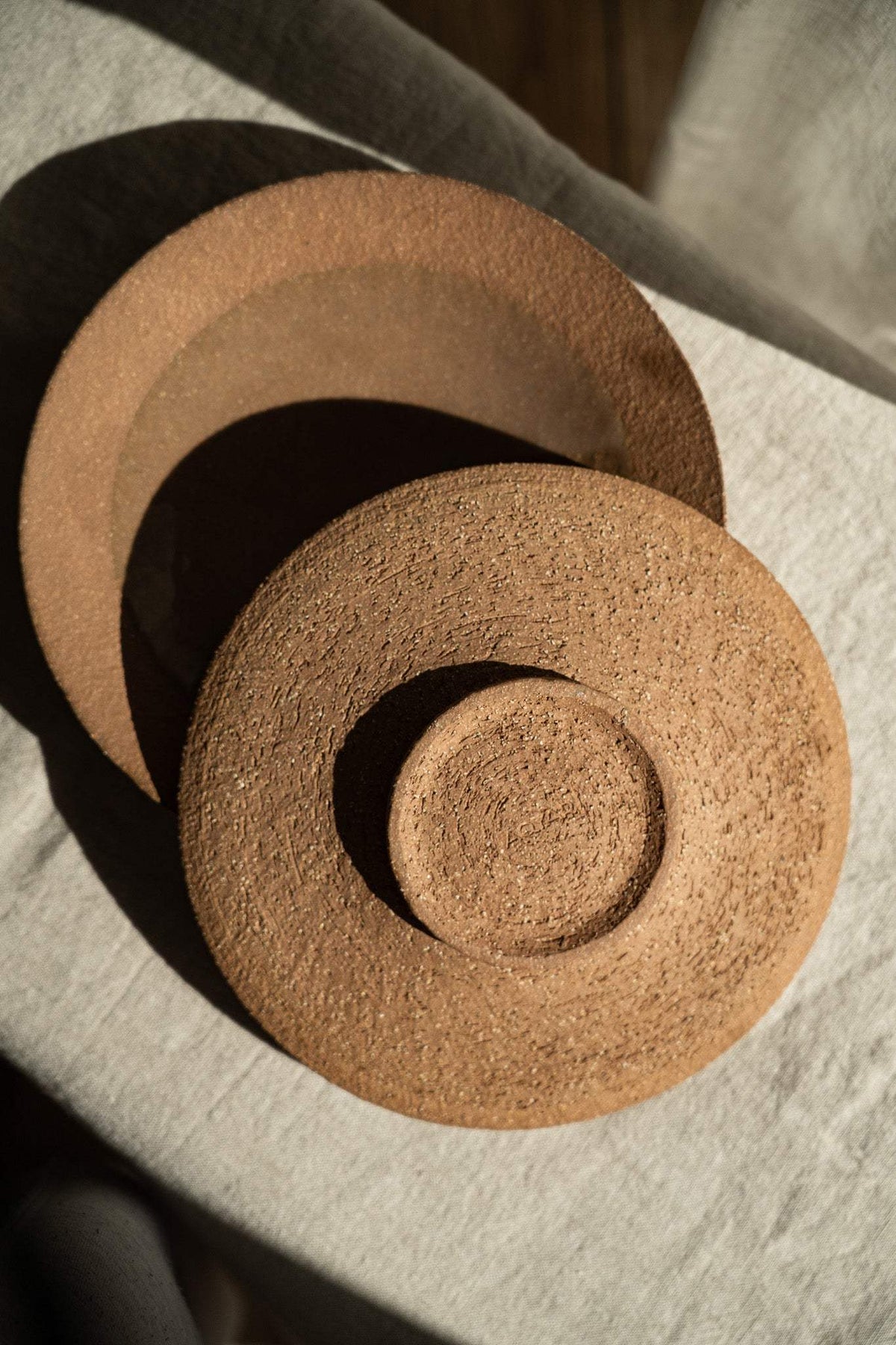 Handmade pinkish-red speckled stoneware pedestal plate with glossy center and unglazed rim