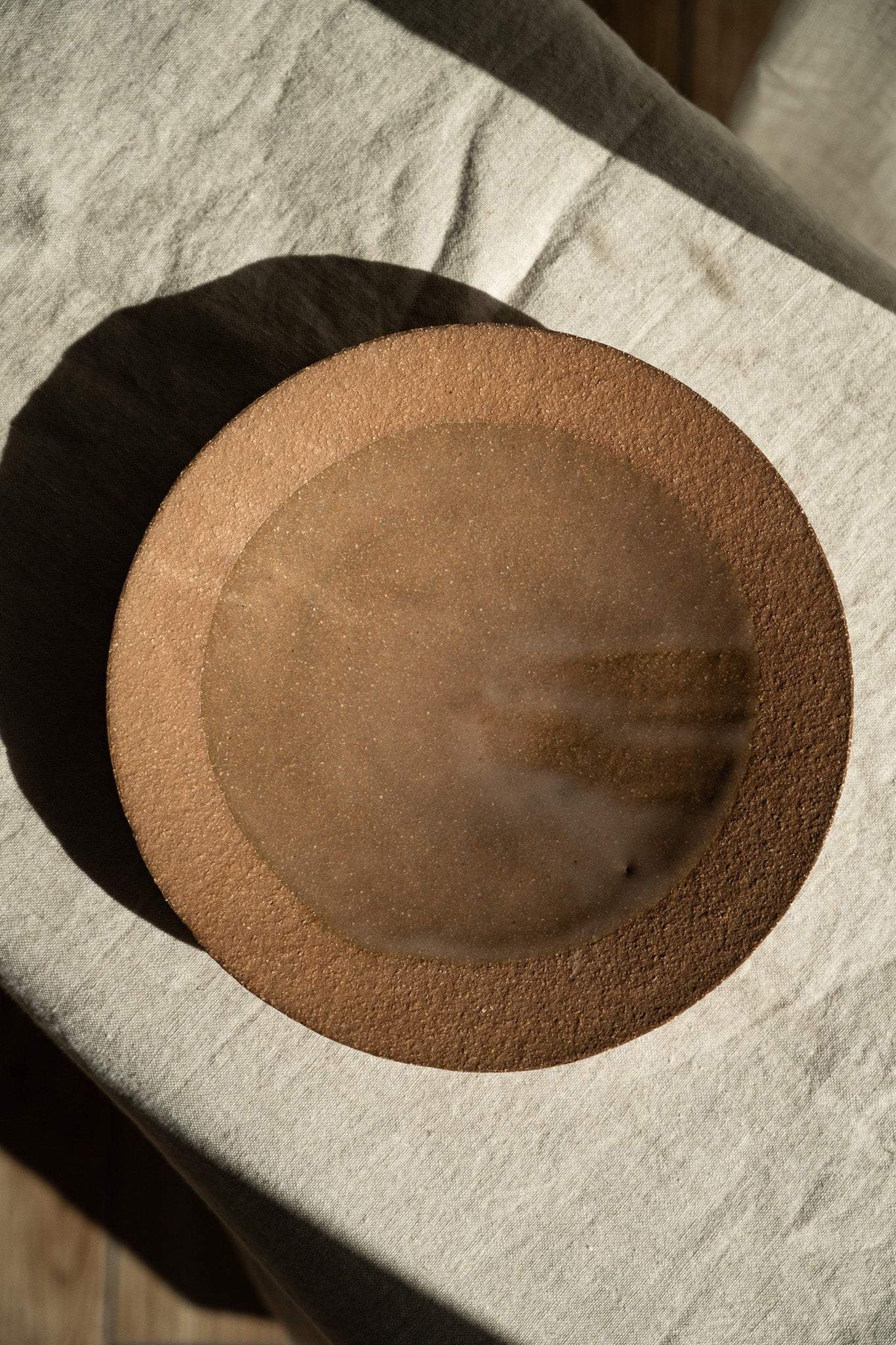Handmade pinkish red stoneware pedestal plate with natural speckles and glossy inner glaze