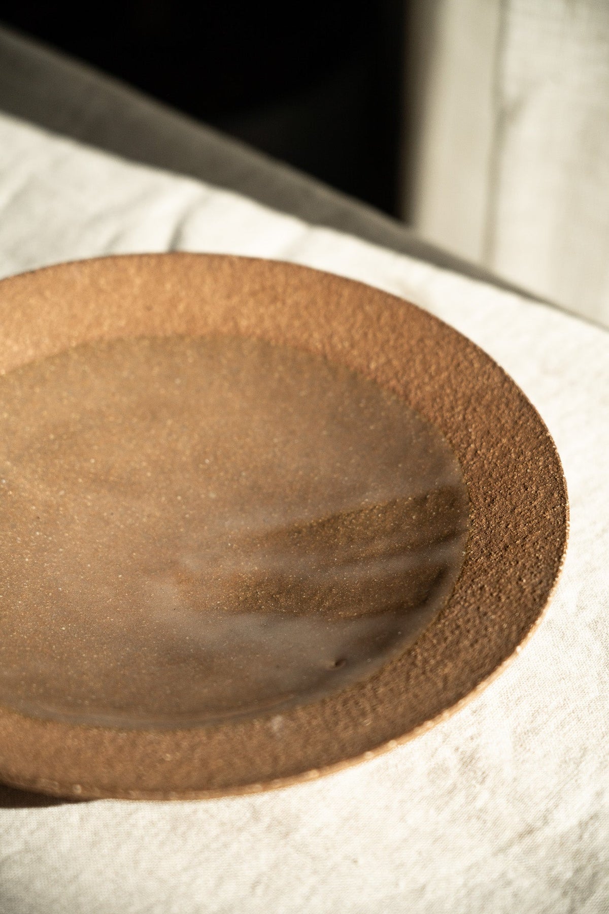 Handmade pinkish-red stoneware pedestal plate with natural speckles and glossy glaze