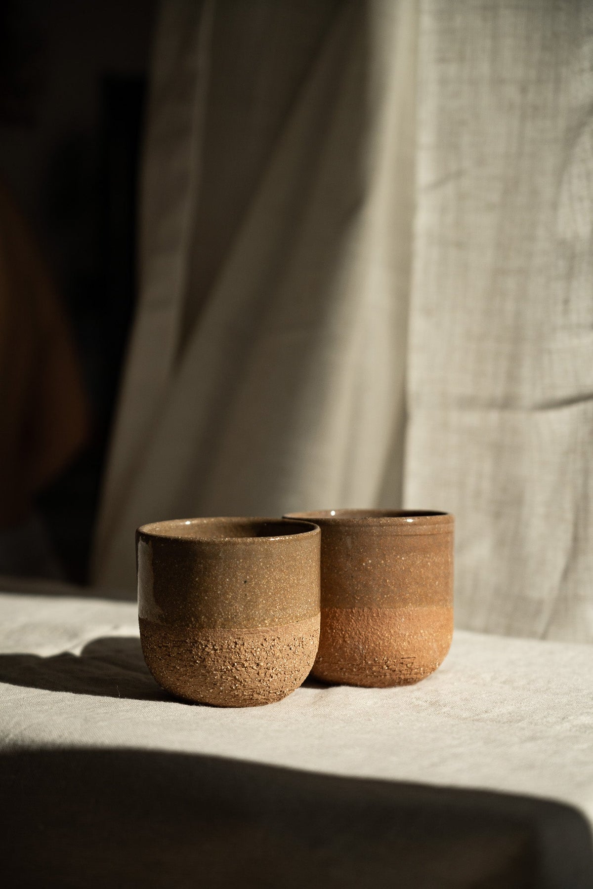 Handmade Pottery Coffee Cup pair in warm brown stoneware with speckled, rough-textured lower halves and smooth rims.