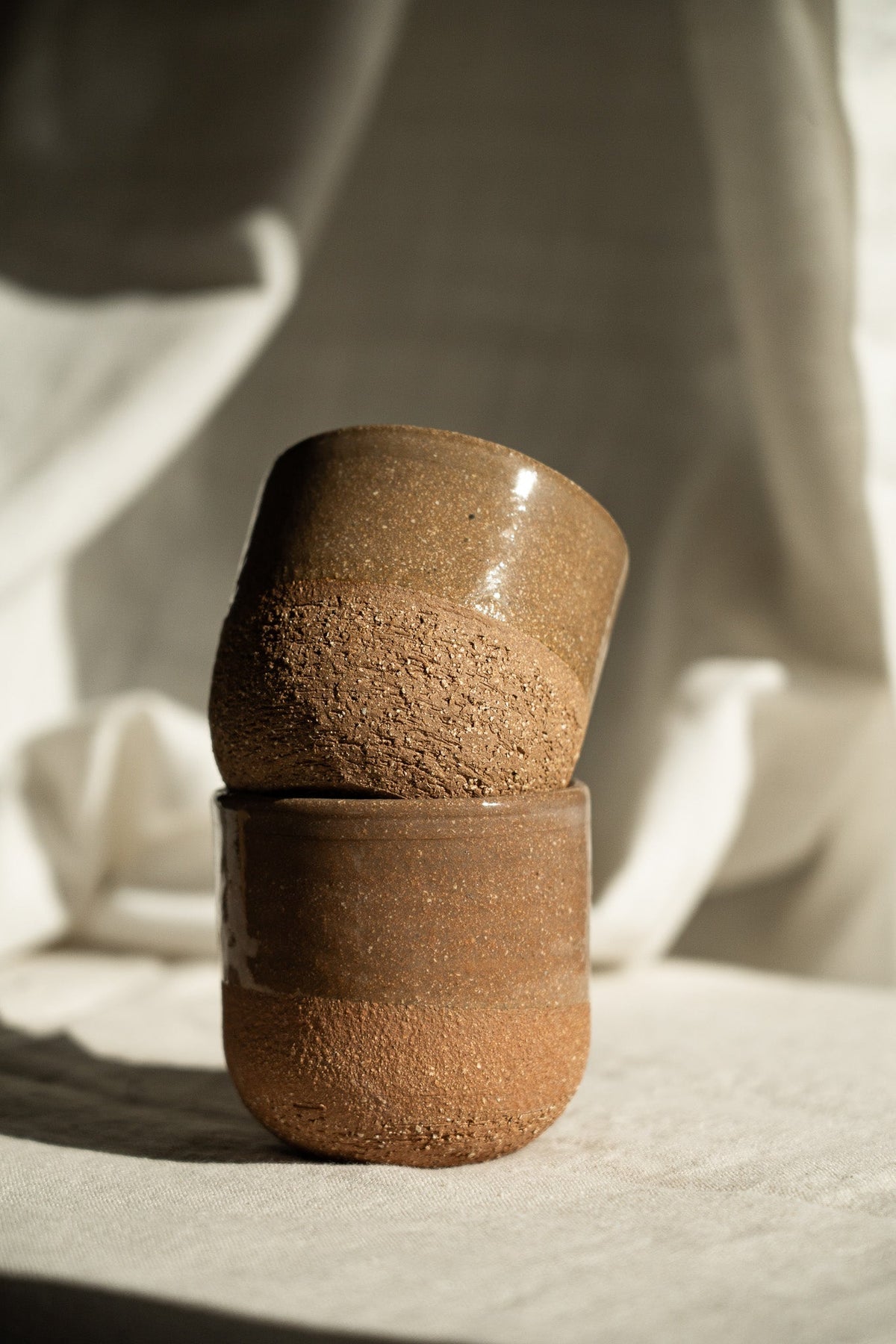 Handmade Pottery Coffee Cup in warm brown stoneware, with a glossy upper glaze and a rough, speckled lower texture.