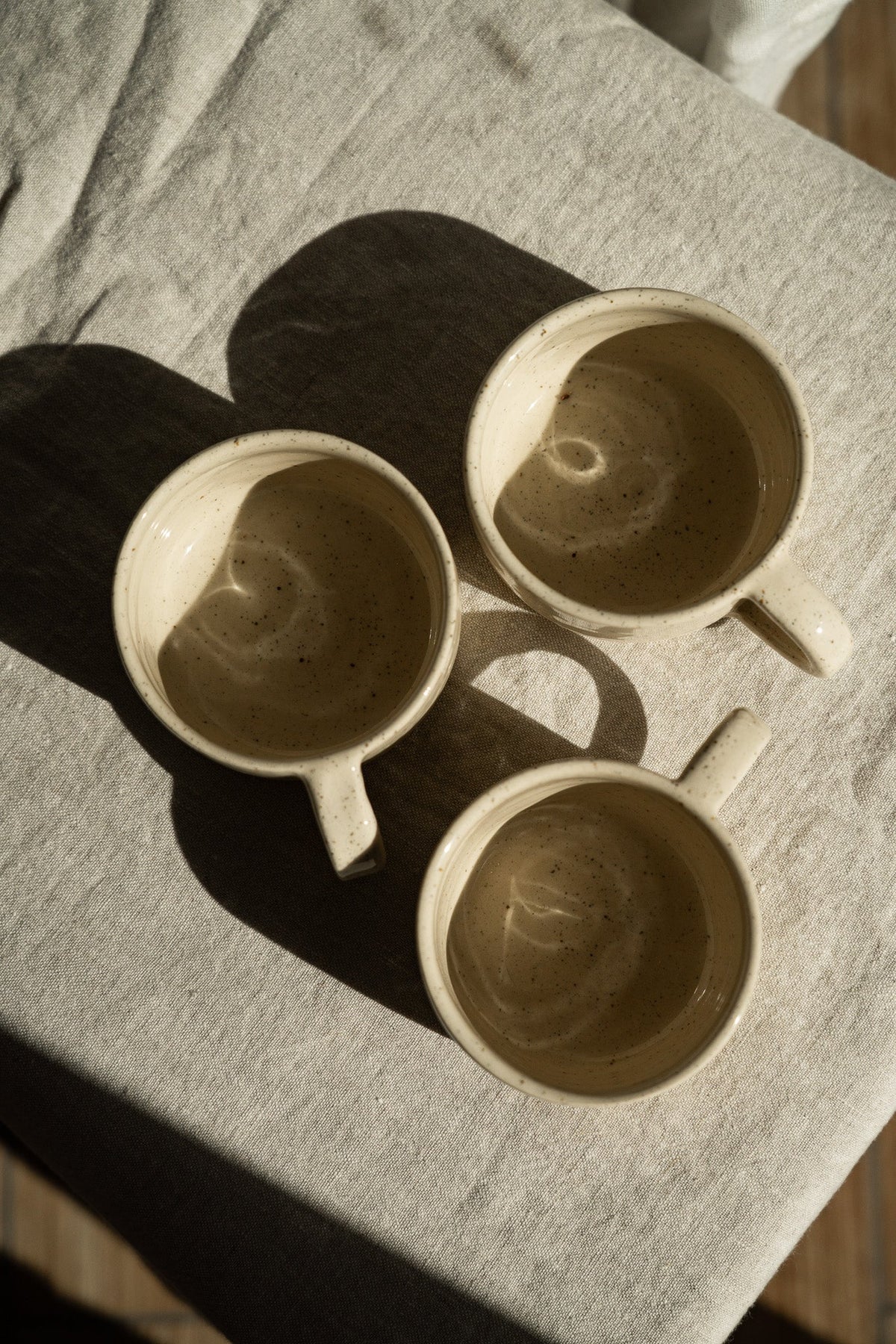 Handmade Stoneware Mug in a warm white sand glaze with fine dark speckles, rounded shape, and curved handle.