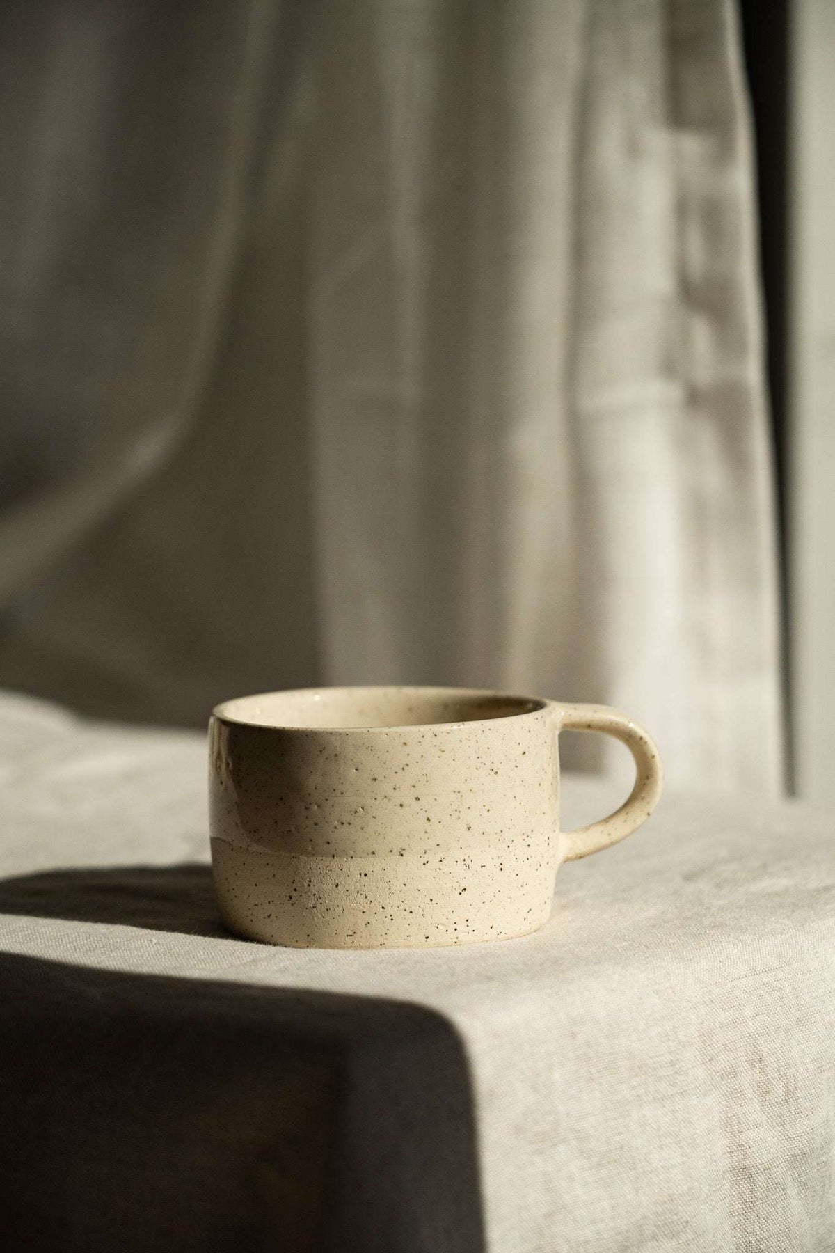 Handmade Stoneware Mug in warm cream with fine brown speckles, a rounded shape, and a curved handle.