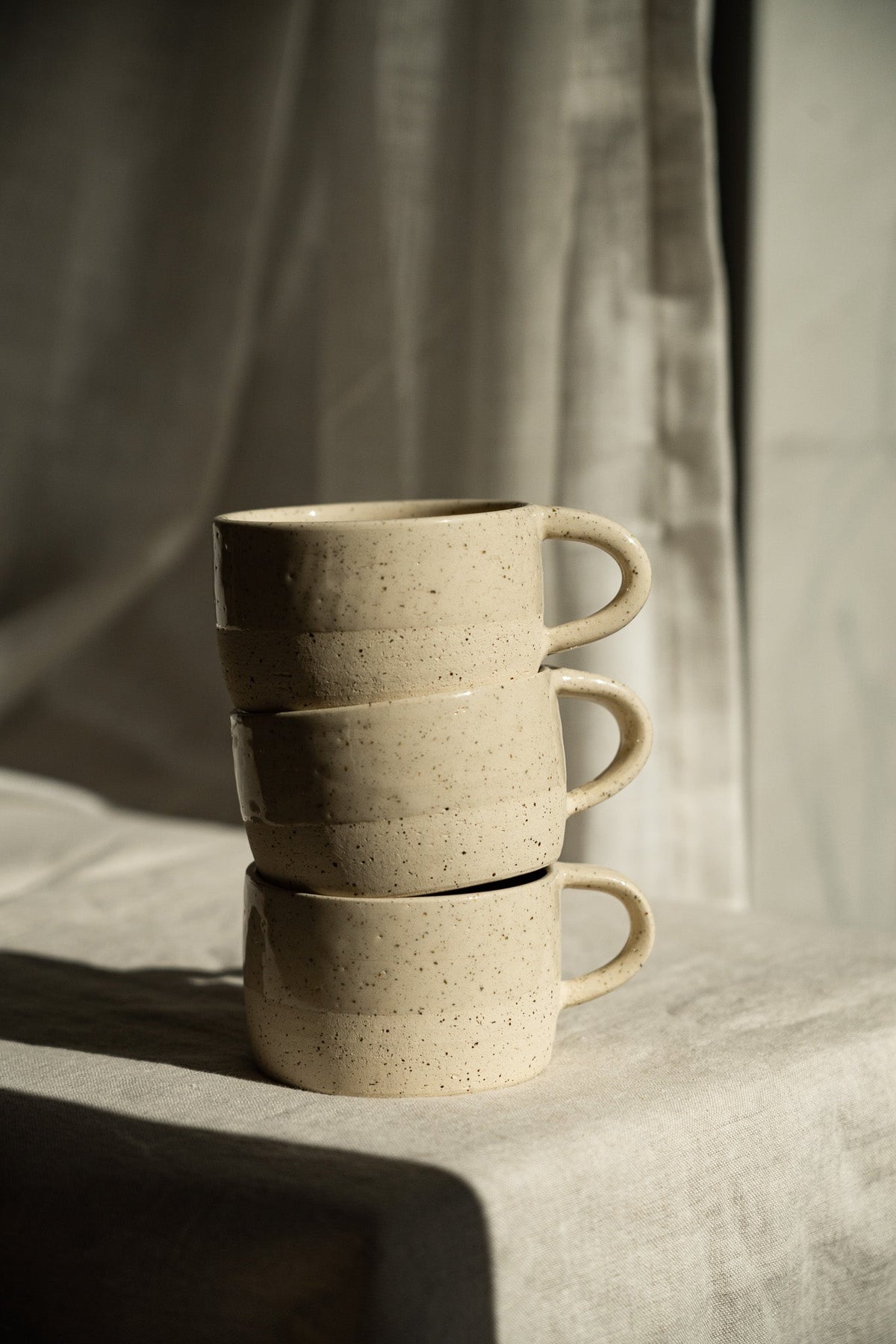 Handmade Stoneware Mug in warm white sand stoneware with fine dark speckles, glossy glaze and rounded handle.