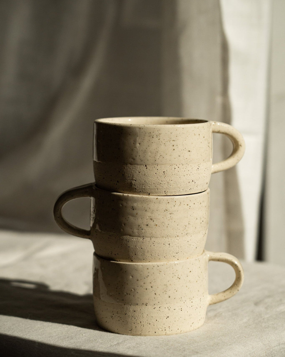 Handmade Stoneware Mug in warm beige with dark speckles, stacked in a trio with rounded handles and a matte finish.
