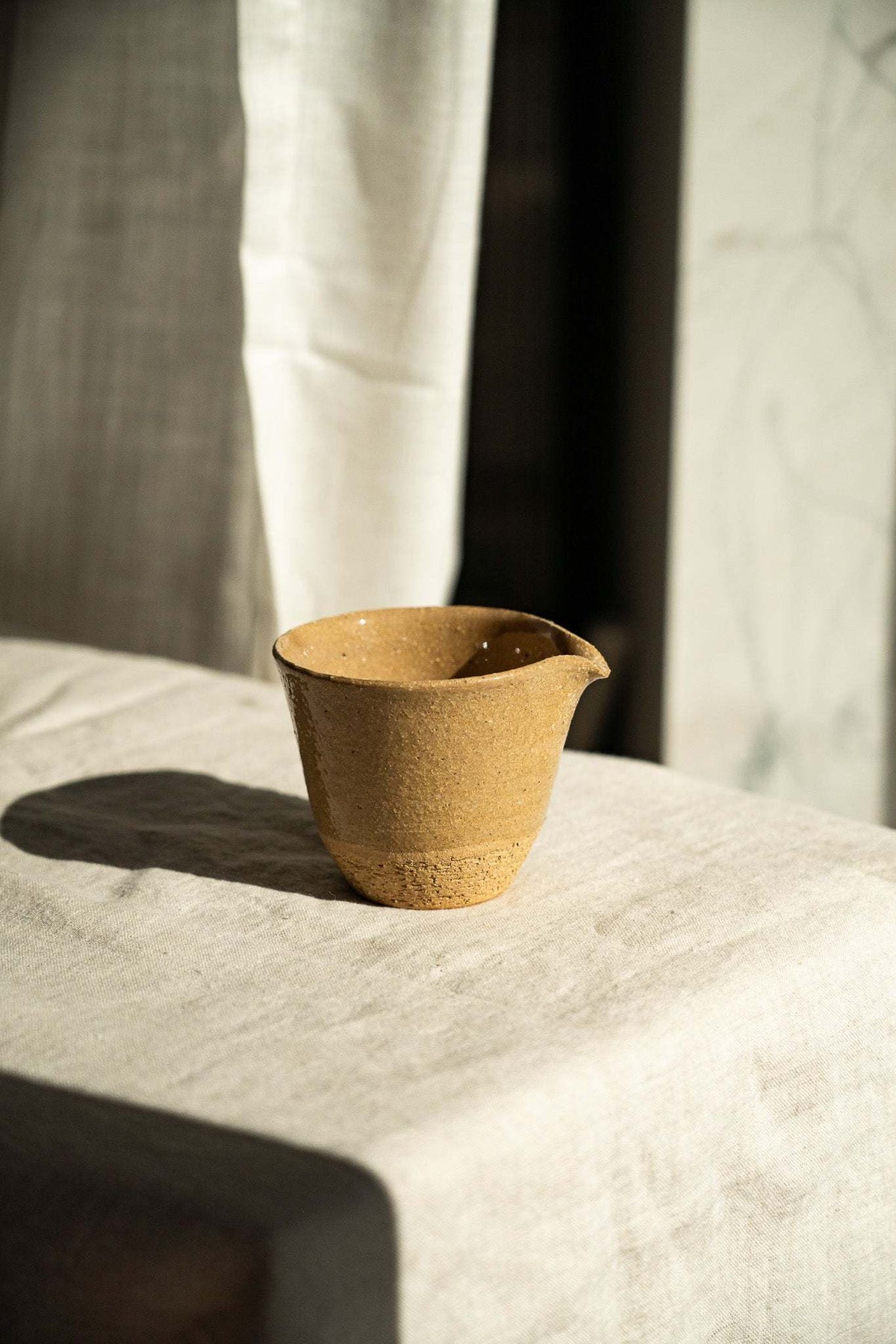 Handmade Stoneware Fair Teacup in warm ochre yellow with fine dark speckles, glossy finish, and a handleless pouring spout.