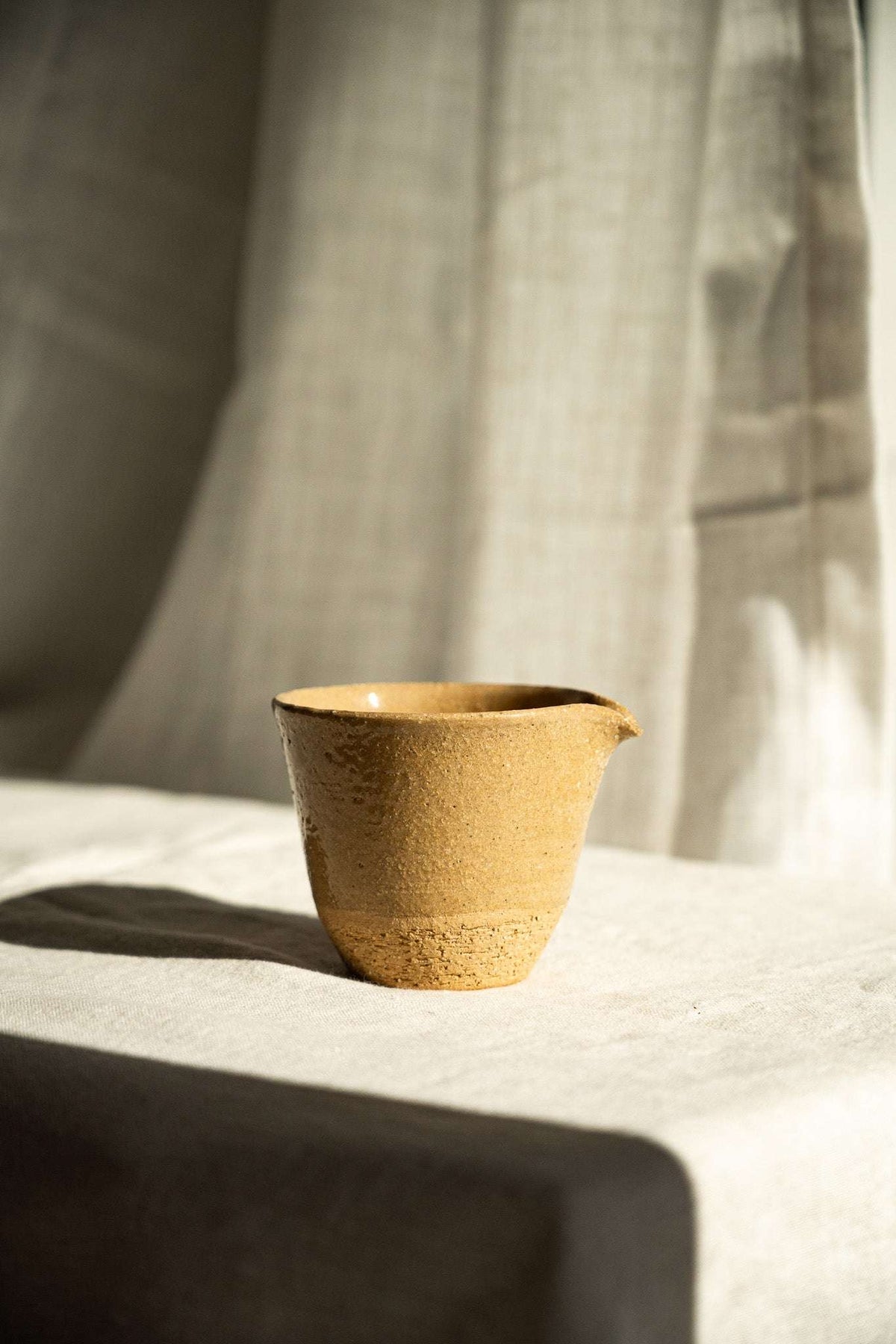 Handmade Stoneware Fair Teacup in warm ochre yellow with a speckled glaze, rounded body, and small pouring spout.