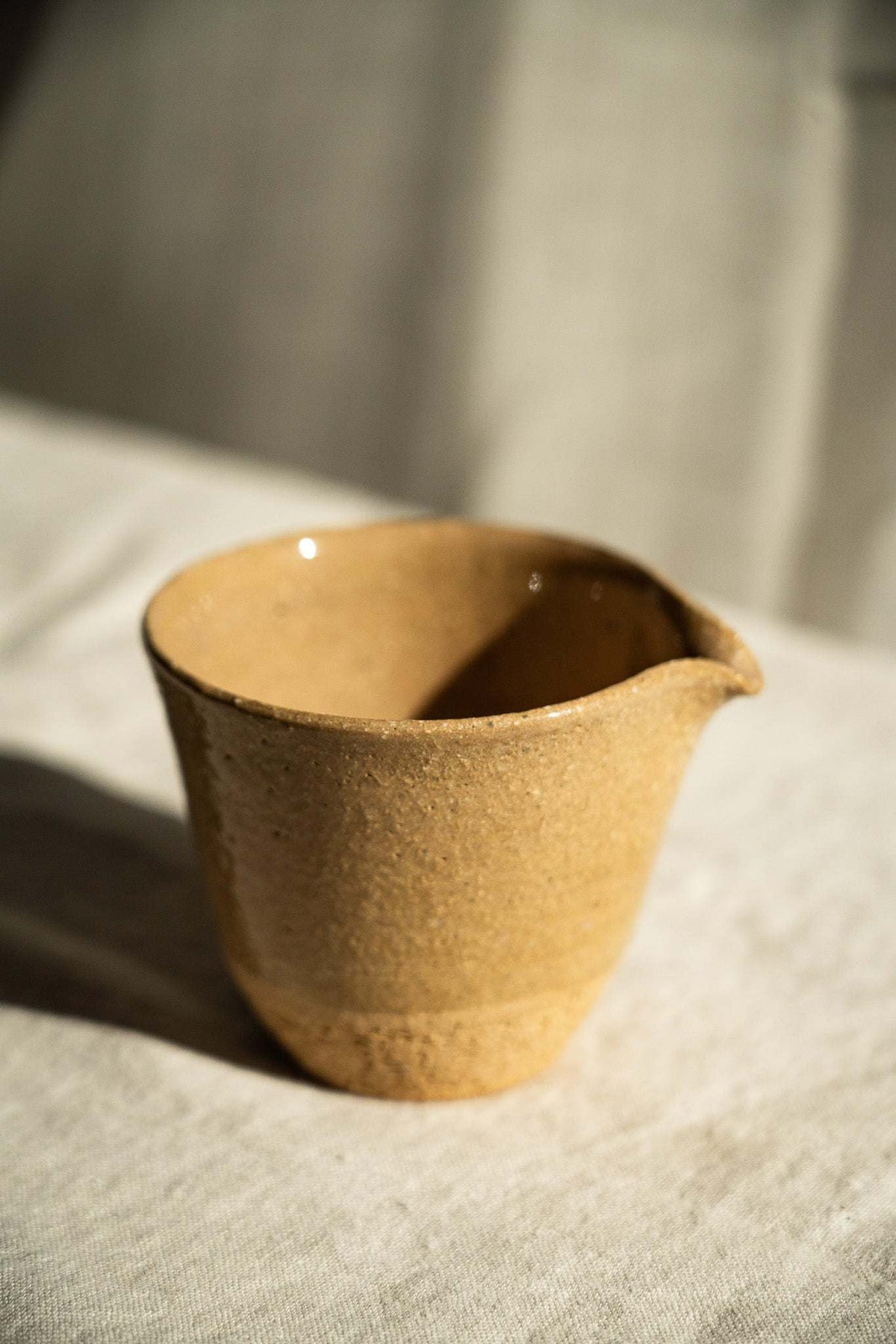 Handmade Stoneware Fair Teacup in warm golden yellow with fine speckles, glossy glaze, and a handleless pouring spout.
