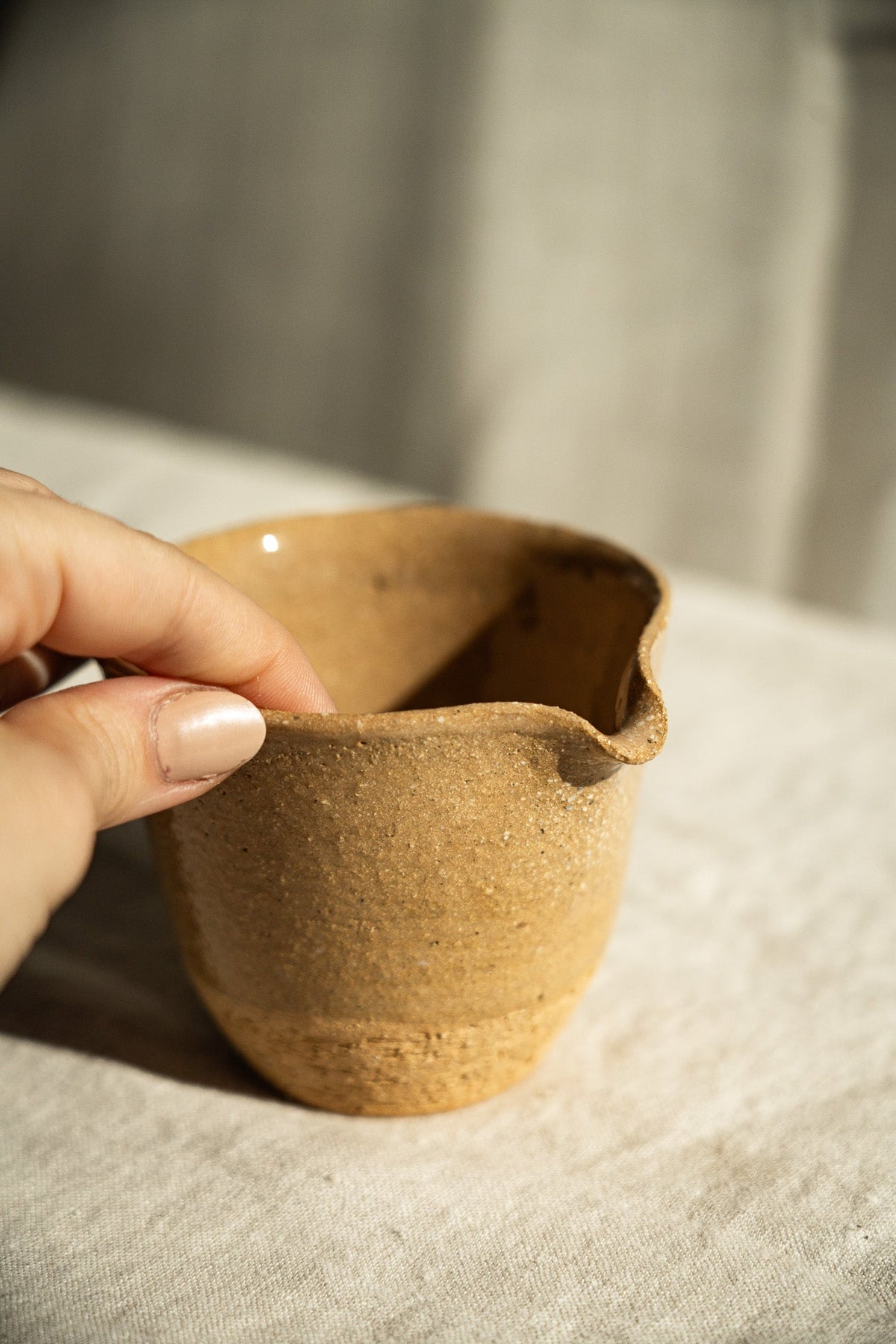 Handmade Stoneware Fair Teacup in warm golden-brown clay with fine speckles, a glossy glaze, and a handleless pouring spout.