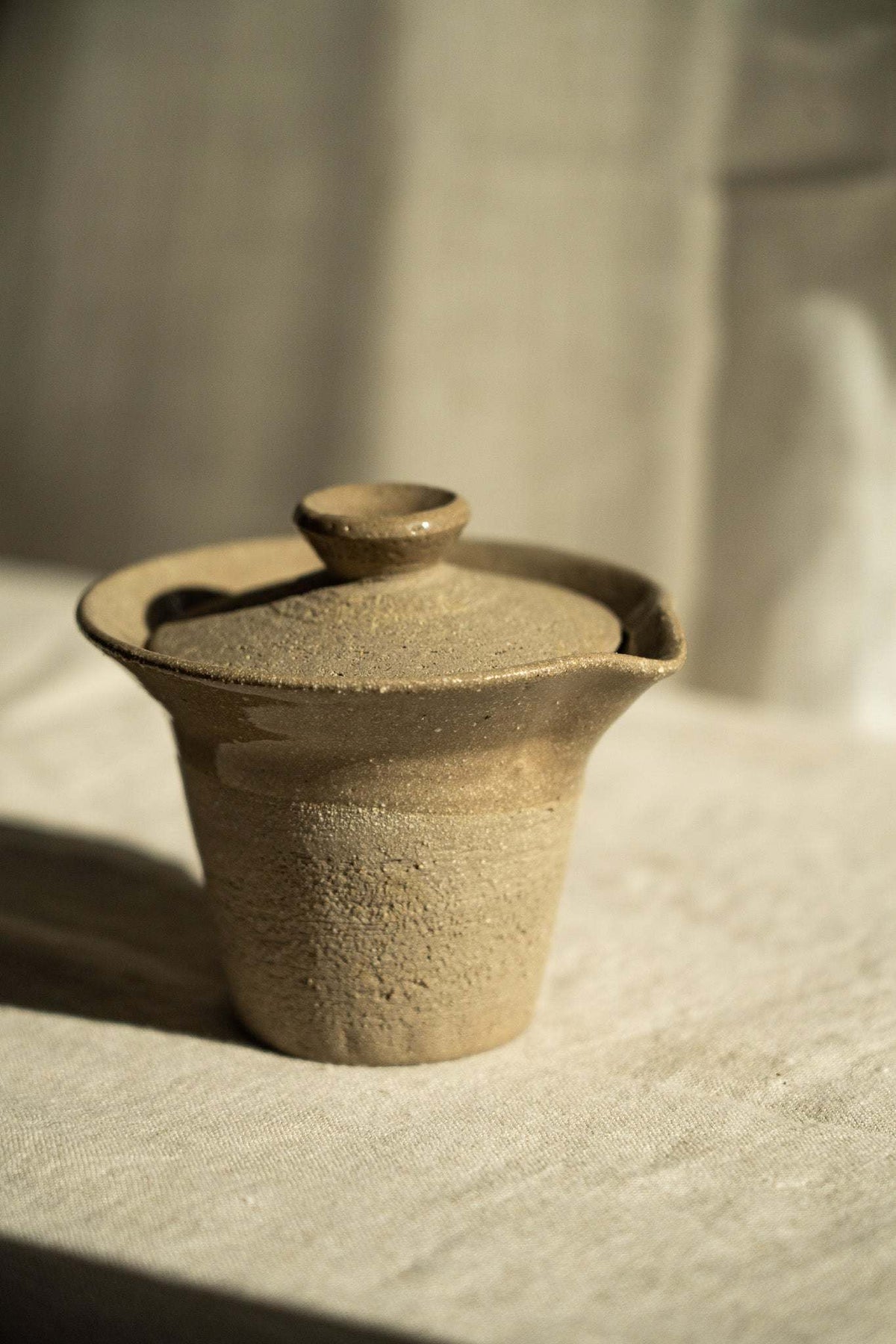 Handmade Stoneware Gaiwan in sandy gray-brown with fine speckles and a fitted lid, flared rim, and pouring spout.