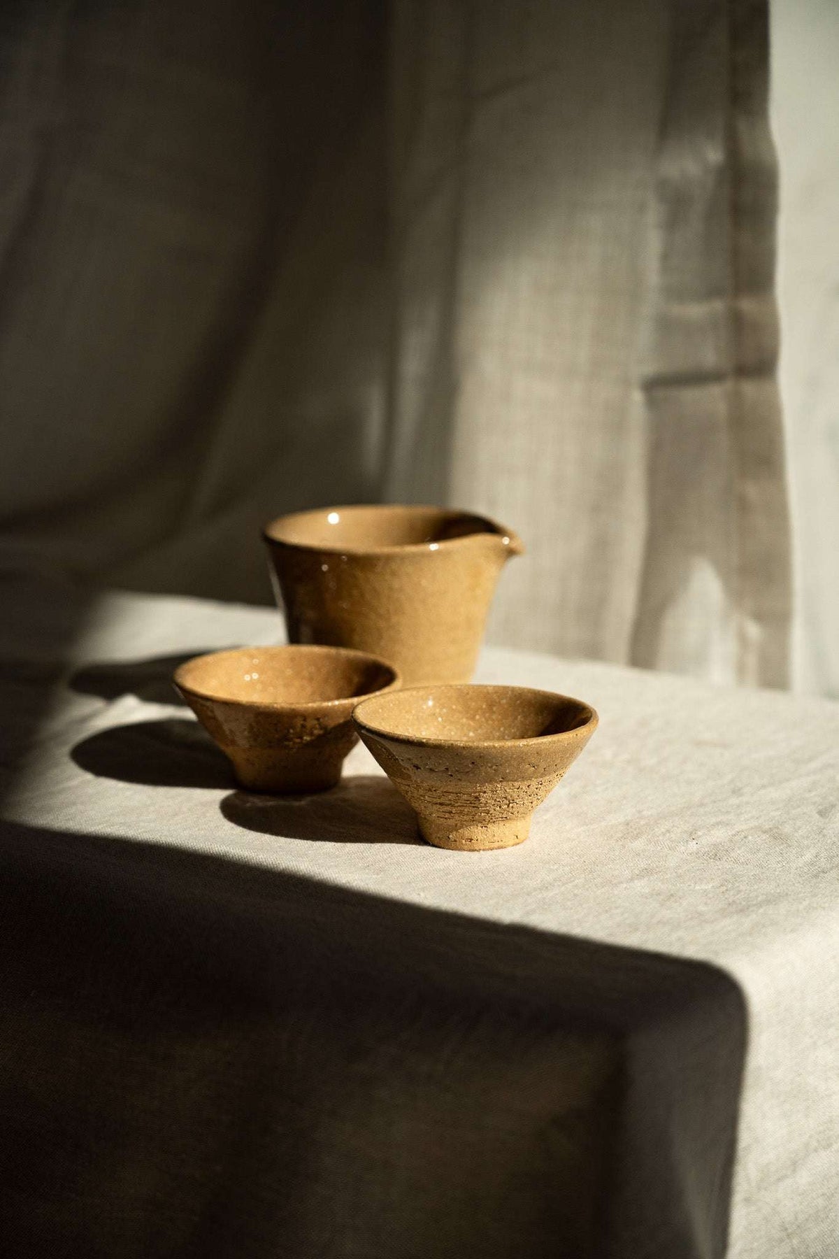 Handmade Stoneware Fair Teacup set in warm ochre-brown glaze with fine speckles, featuring a handleless pitcher and two cups.