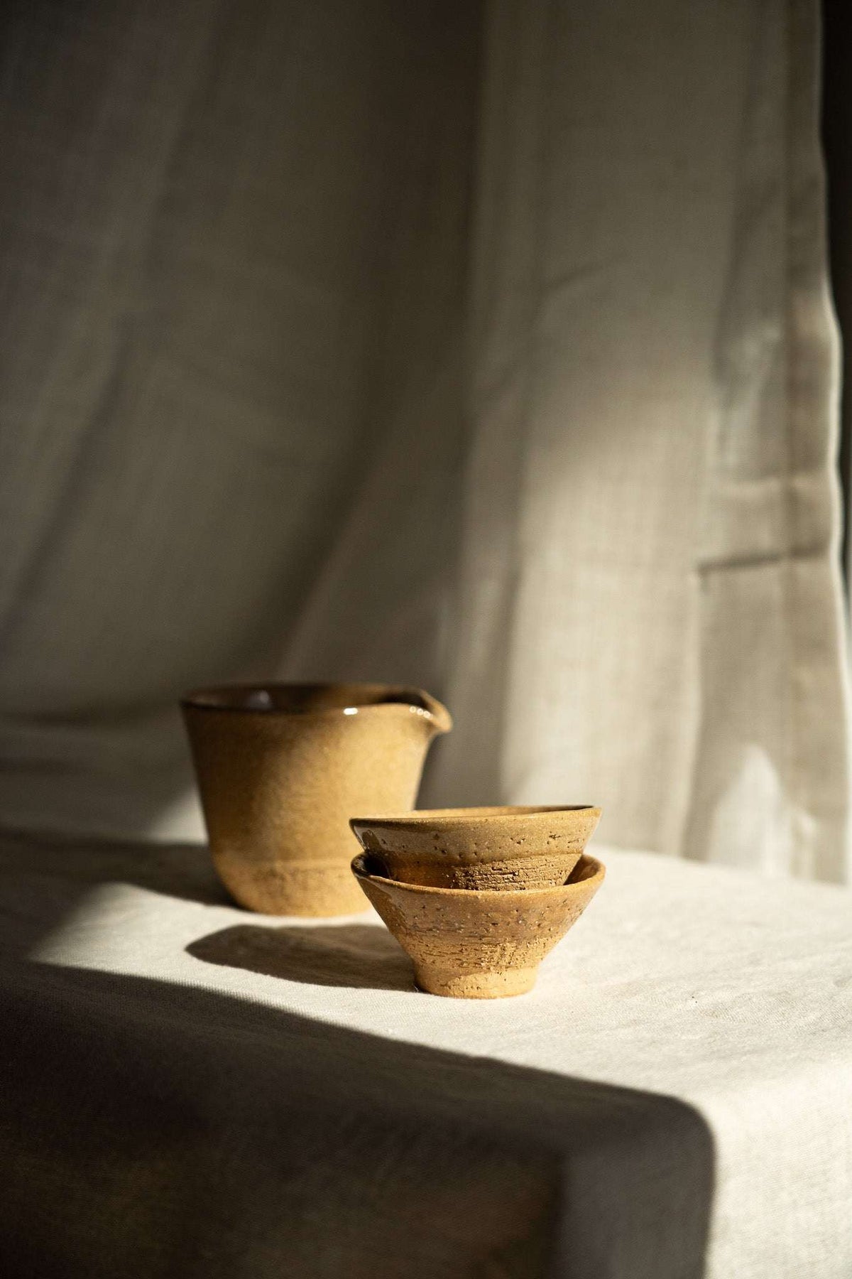 Handmade Stoneware Fair Teacup set in warm ochre yellow with dark speckles, glossy glaze, and handleless forms.