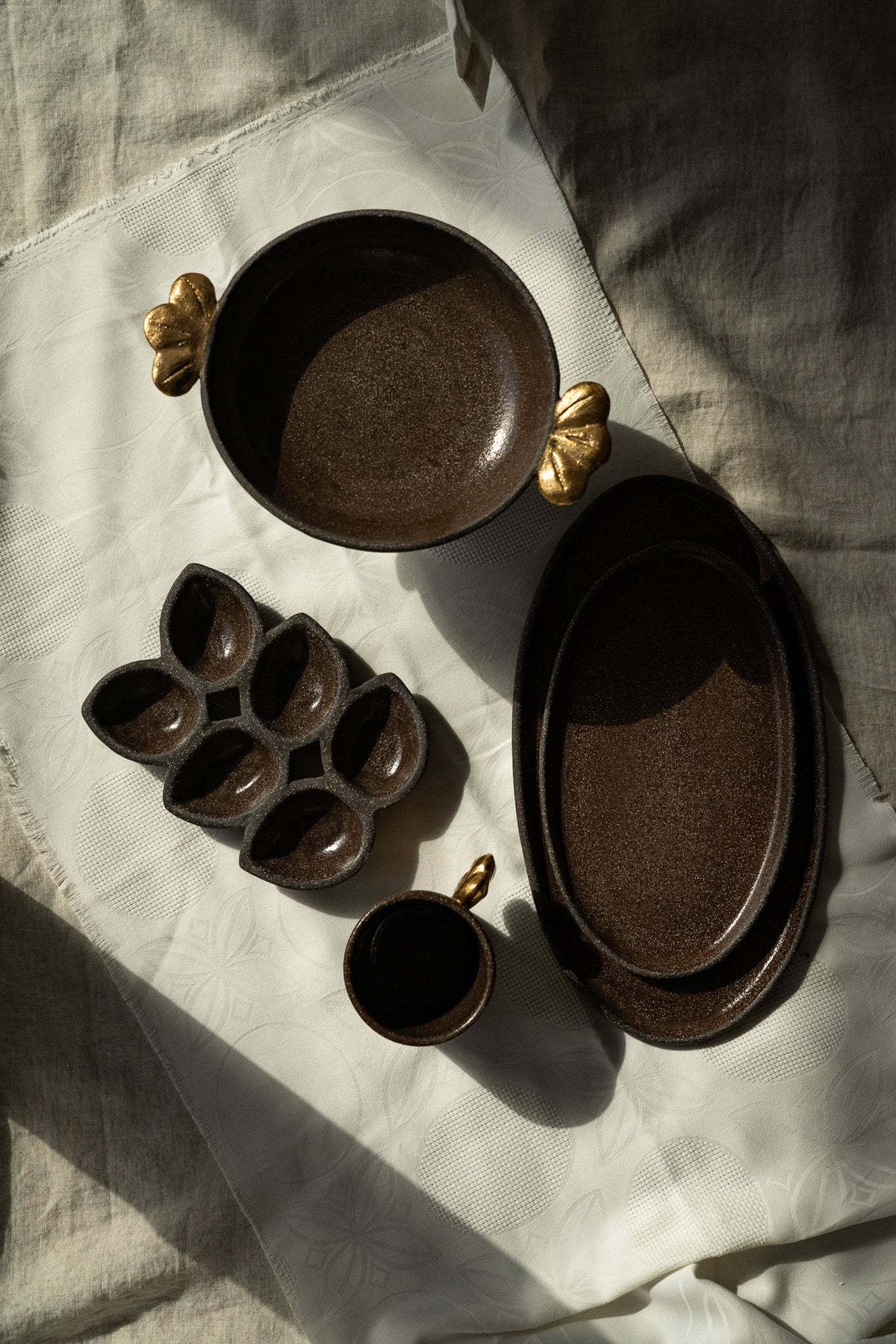 Stoneware pedestal fruit bowl in dark brown with a rough-textured finish and sculptural gold leaf accents on each side.