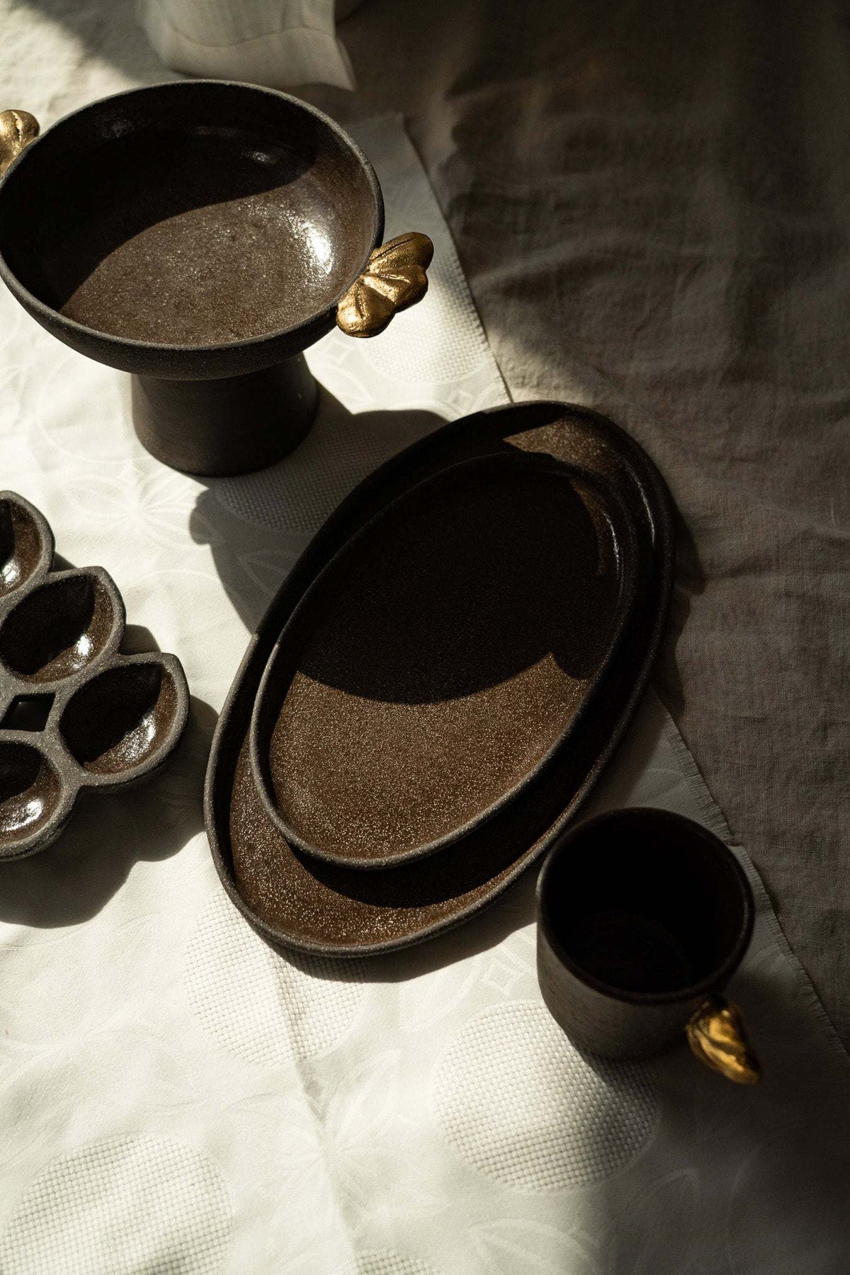 Pedestal fruit bowl in dark brown textured stoneware with a smooth glazed interior and small gold leaf accents.