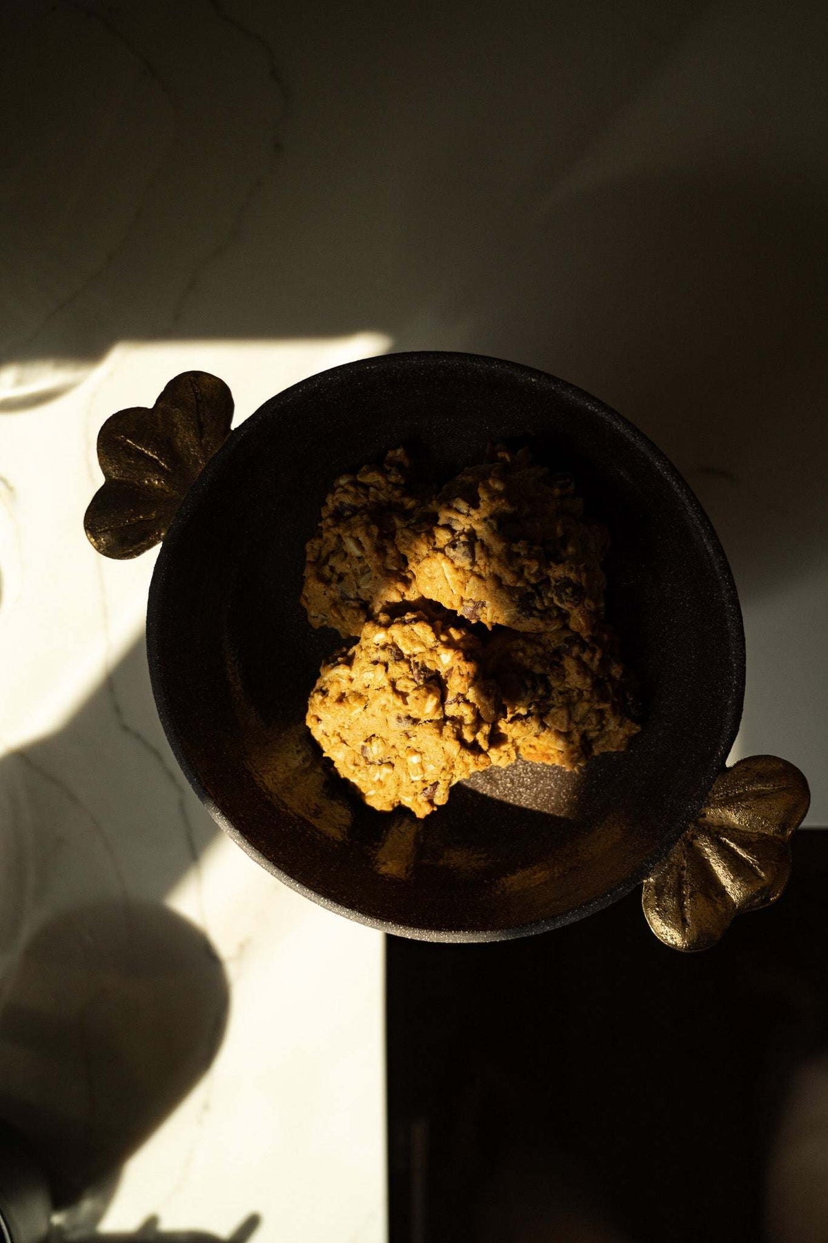 Pedestal fruit bowl in dark charcoal stoneware with a matte textured exterior, smooth interior, and gold leaf accents.