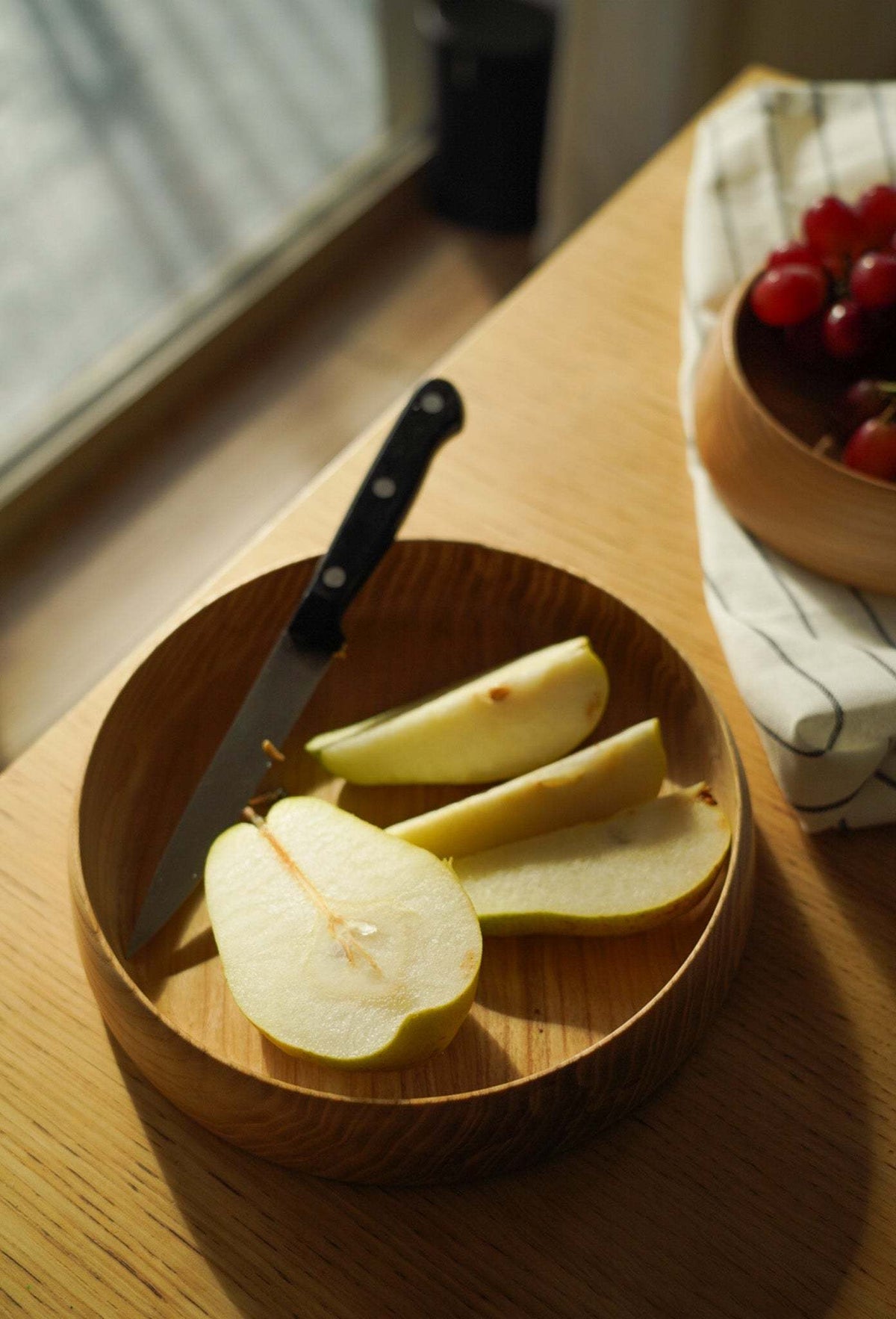 Hand Carved Wooden Plate in warm brown wood, with natural grain, a round shape and high carved sides, holding sliced pears