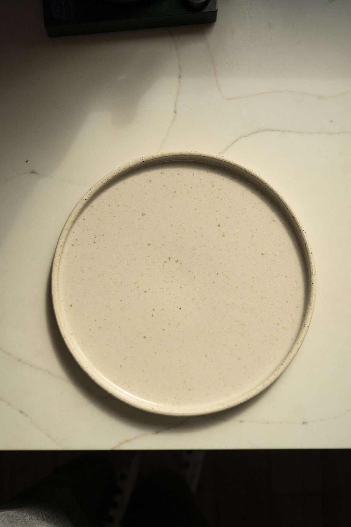 Stoneware Pottery Plate in creamy white stoneware with fine brown speckles and a raised rim, handmade with a smooth glazed center.