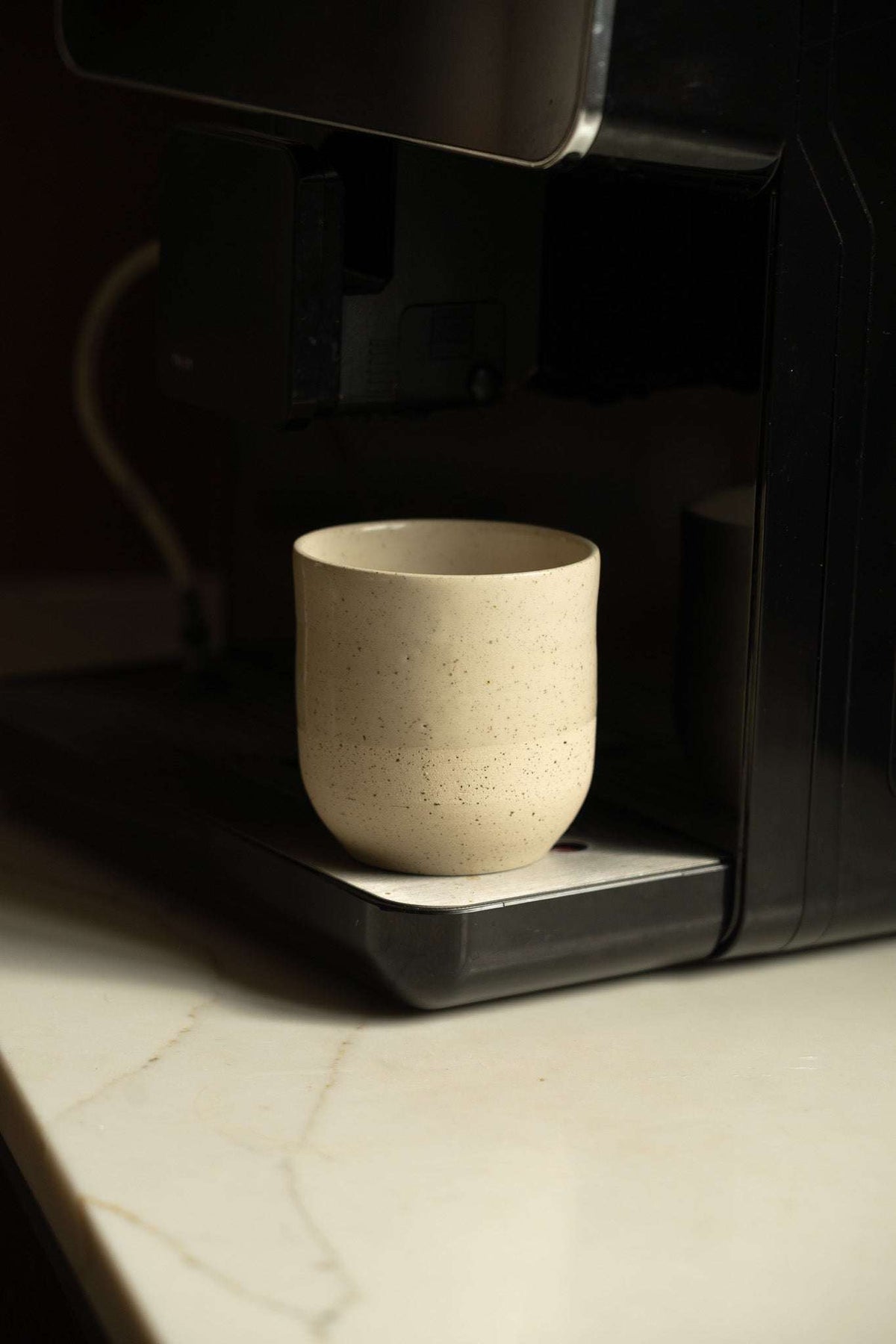 Small Coffee Cup in cream-white speckled stoneware, with a rounded cylindrical shape and smooth, unhandled sides.