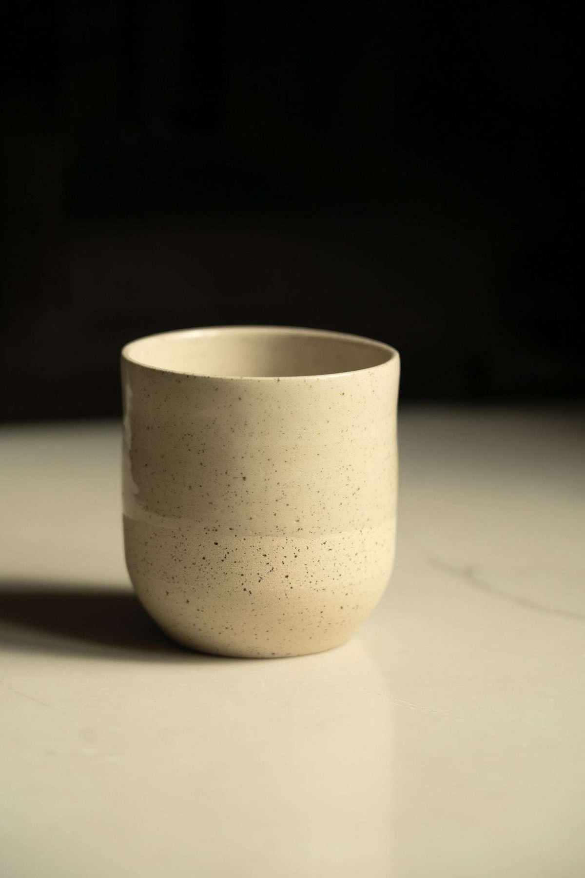 Small Coffee Cup in cream-white speckled stoneware with a simple rounded shape and smooth, unhandled sides.