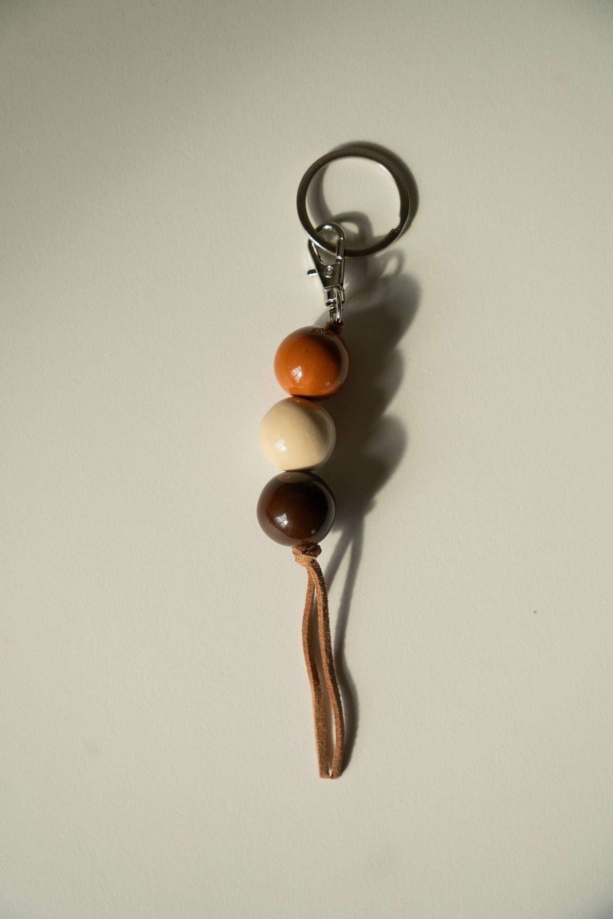 Ceramic Keychain with three glossy ceramic beads in orange, cream, and dark brown, a leather cord, and silver-tone ring.