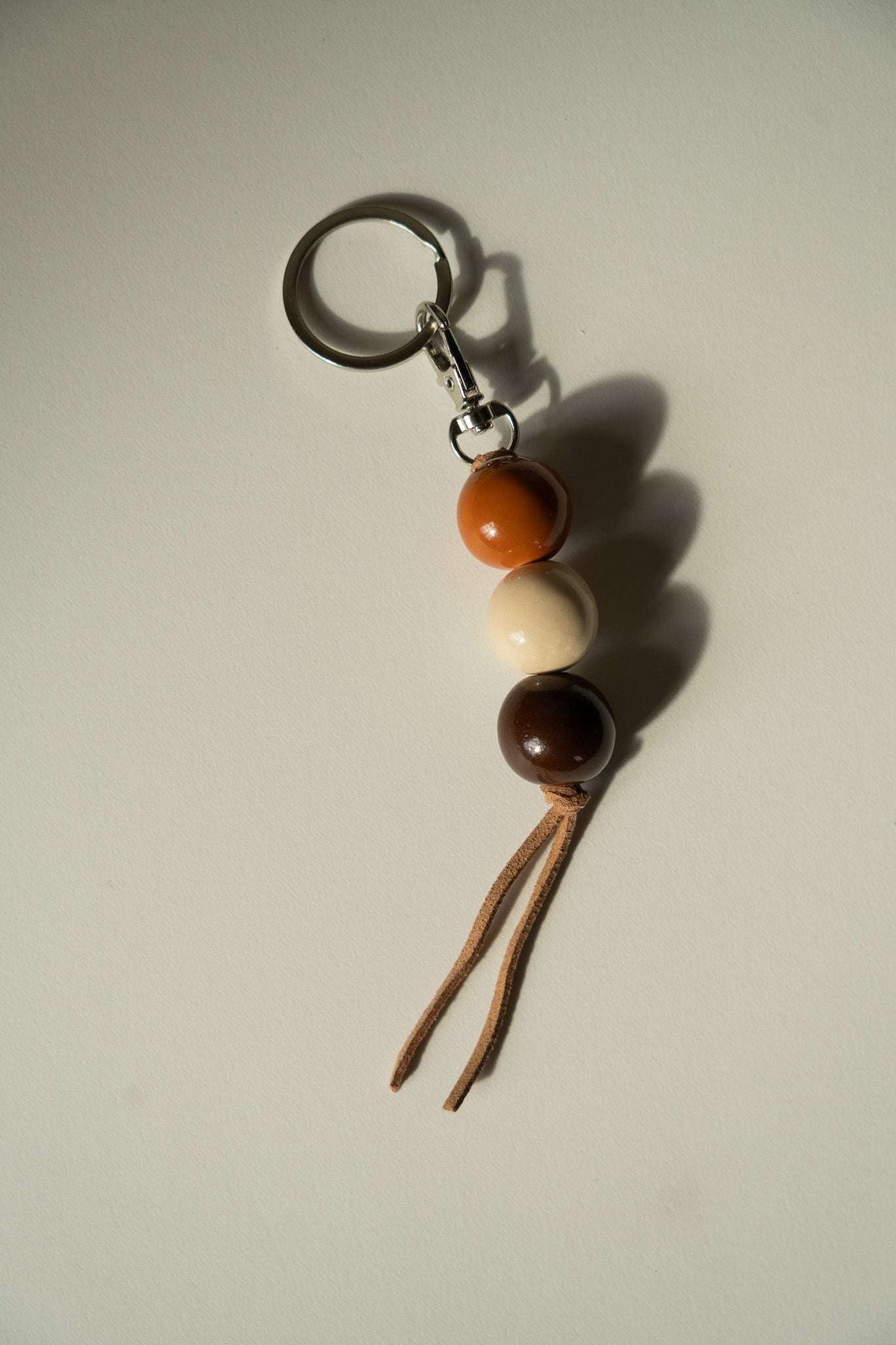 Ceramic Keychain with three glossy orange, cream, and dark brown beads, silver-tone clasp, and split leather cord tails.