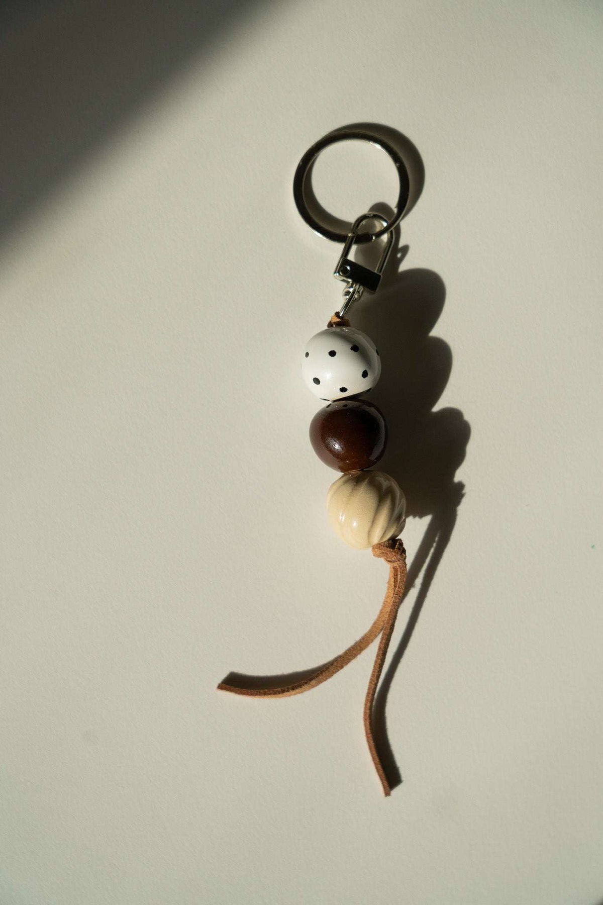 Ceramic Beaded Keychain with white dotted, dark brown, and cream textured beads, brown leather cord, and metal ring.