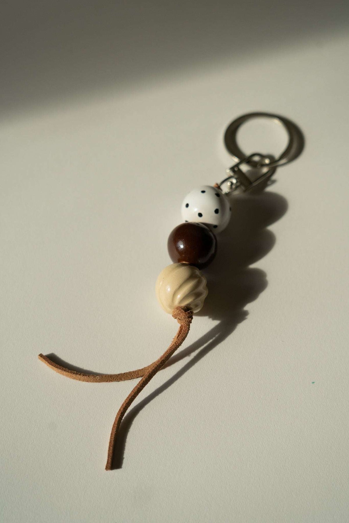 Ceramic Beaded Keychain with white dotted, dark brown and cream ceramic beads, a tan leather cord and silver-tone clasp.