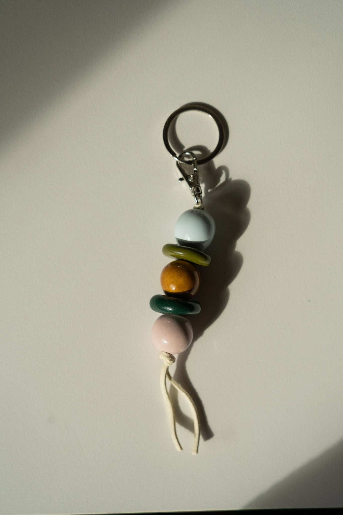 Beaded Keychain with glossy ceramic beads in blue, olive green, amber and pale pink, tied with a cream cord and metal ring.