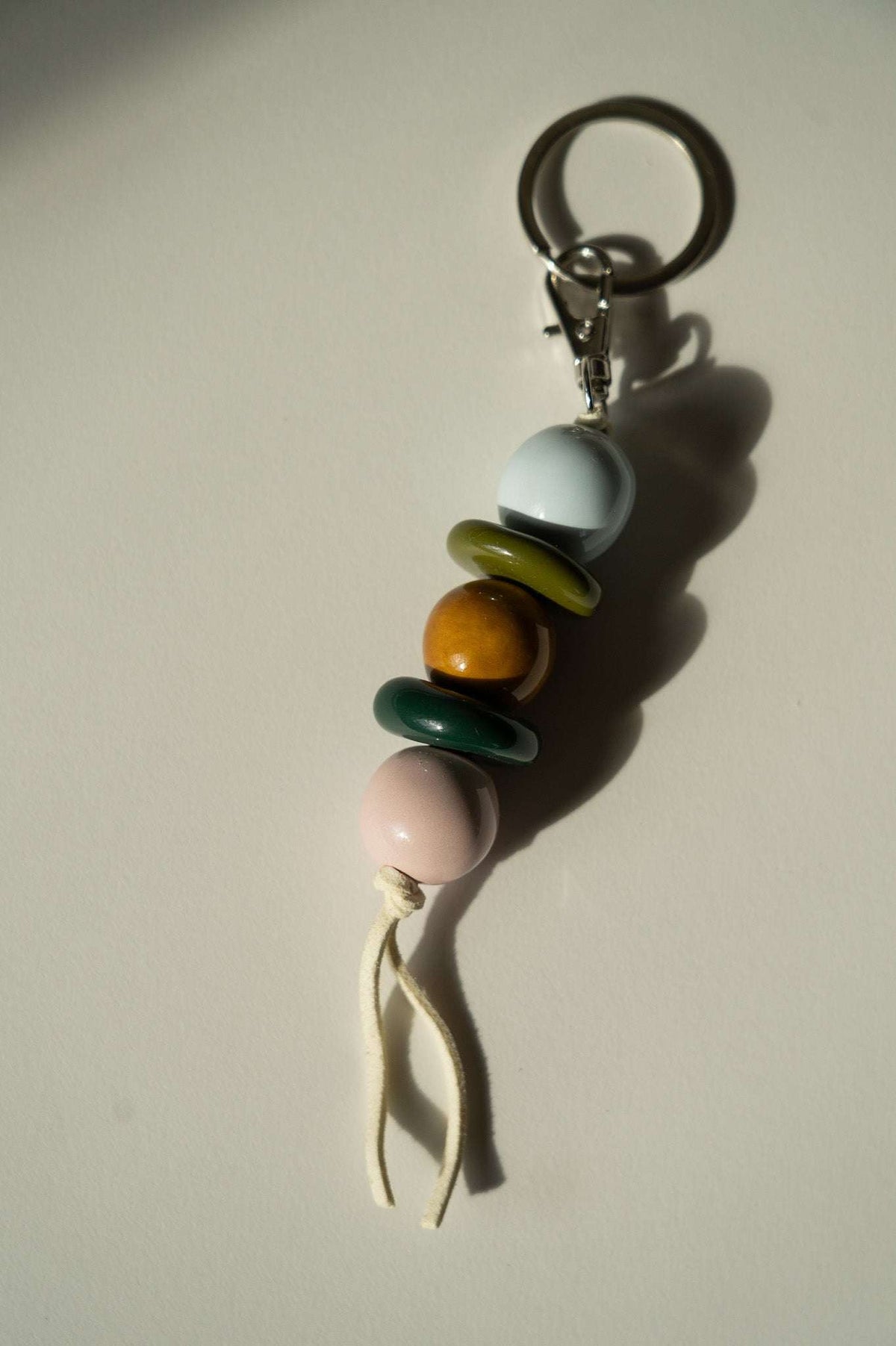 Beaded Keychain with glossy ceramic beads in pale blue, olive, amber, dark green and pink, tied with a cream cord.