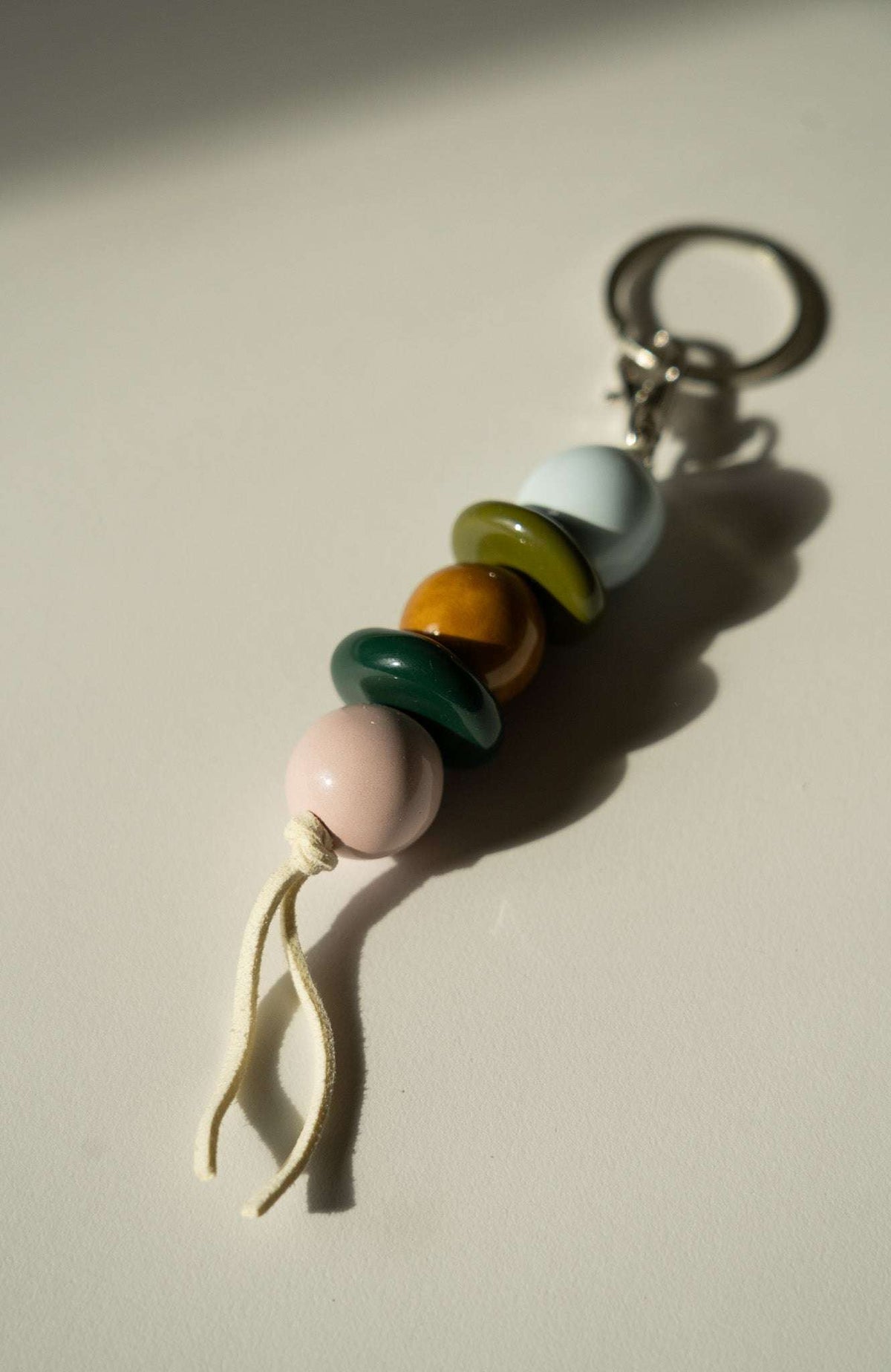 Beaded Keychain with glossy ceramic beads in pale pink, teal, amber, olive and white, tied with a cream cord and metal ring.