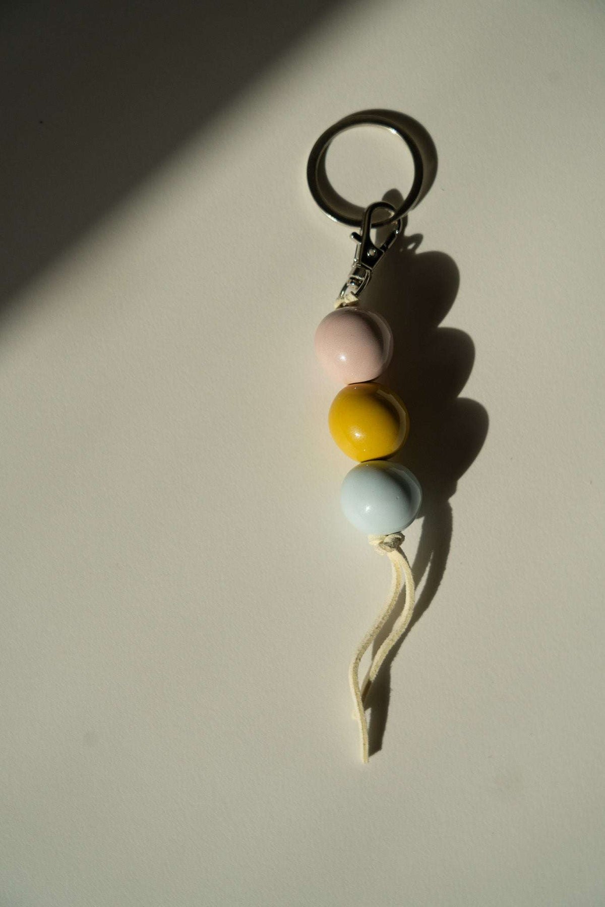Ceramic Beaded Keychain with pink, mustard yellow, and pale blue round beads, metal clasp, and cream cord.