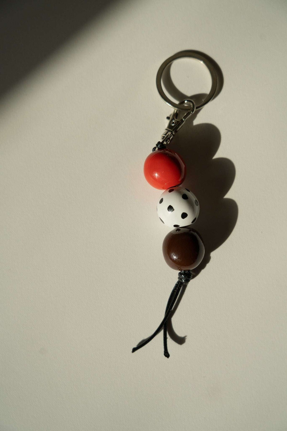 Beaded Keychain with glossy red and brown ceramic beads, a white spotted bead, dark leather cord and silver-tone hardware.