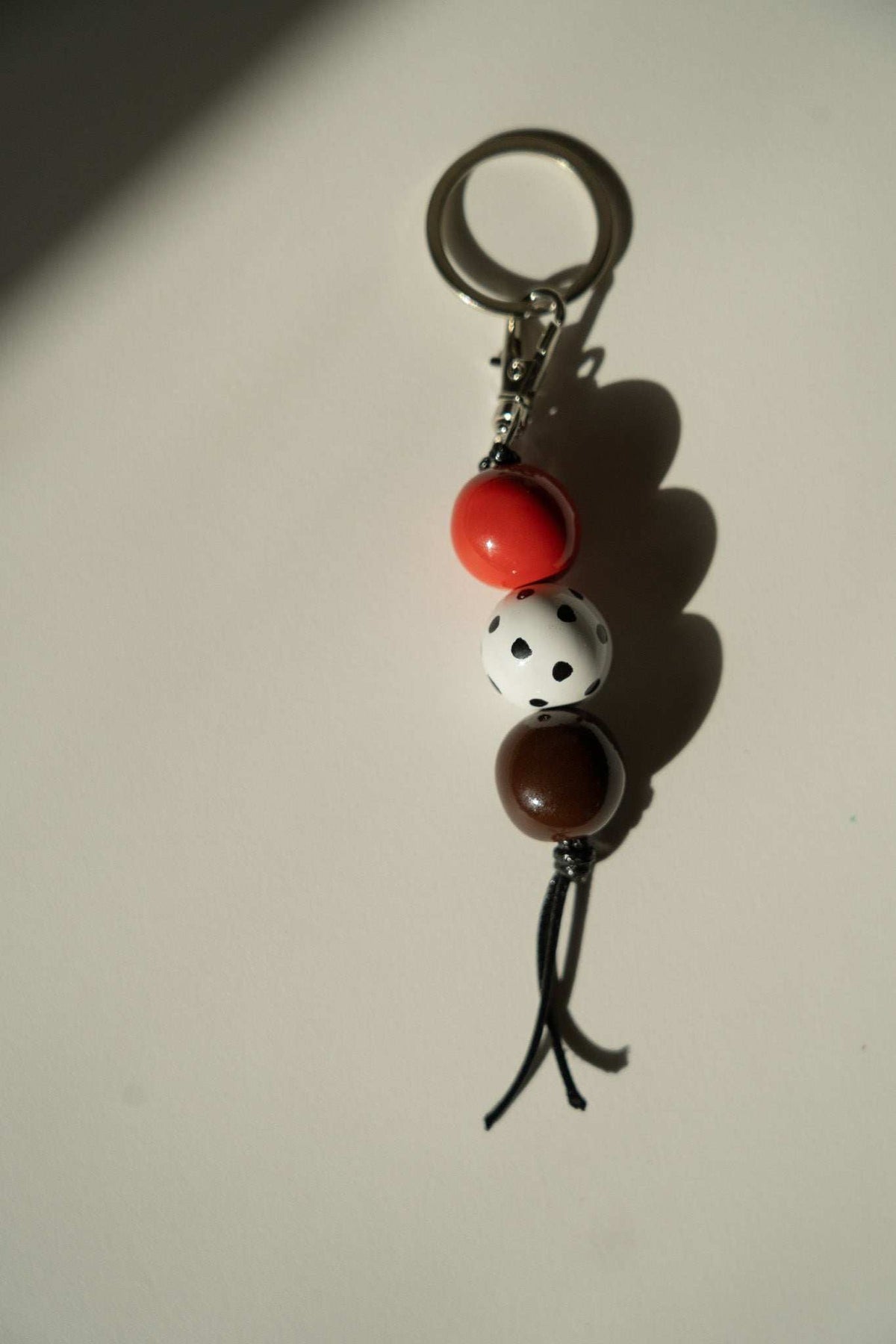 Beaded Keychain with glossy red, white black-spotted, and brown ceramic beads, silver-tone ring, and black cord.