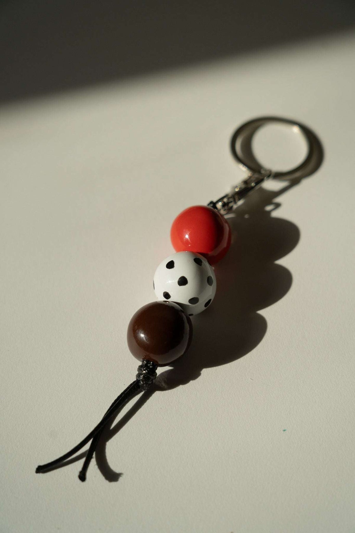 Beaded Keychain with glossy red and brown ceramic beads, a white black-spotted bead, black cord, and silver-tone ring.