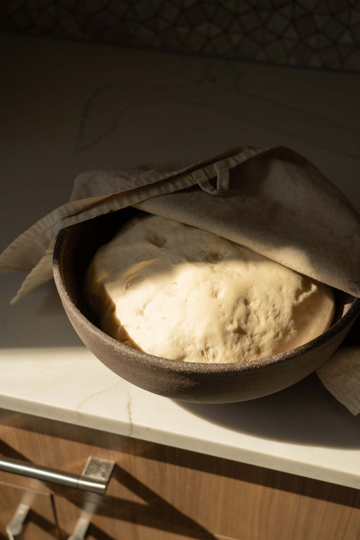 Stoneware Large Fruit Bowl in warm brown with a rough, matte exterior, holding dough beneath a draped cloth.