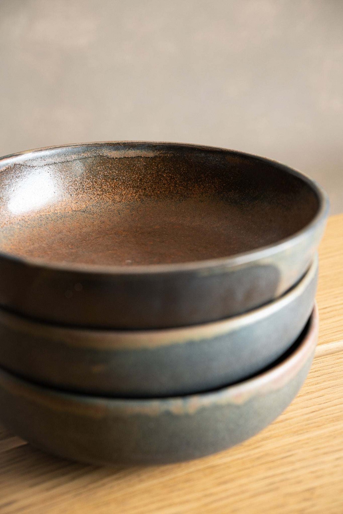 Stoneware pasta bowl in dark charcoal stoneware with a rust-brown speckled reactive glaze and rounded rim.