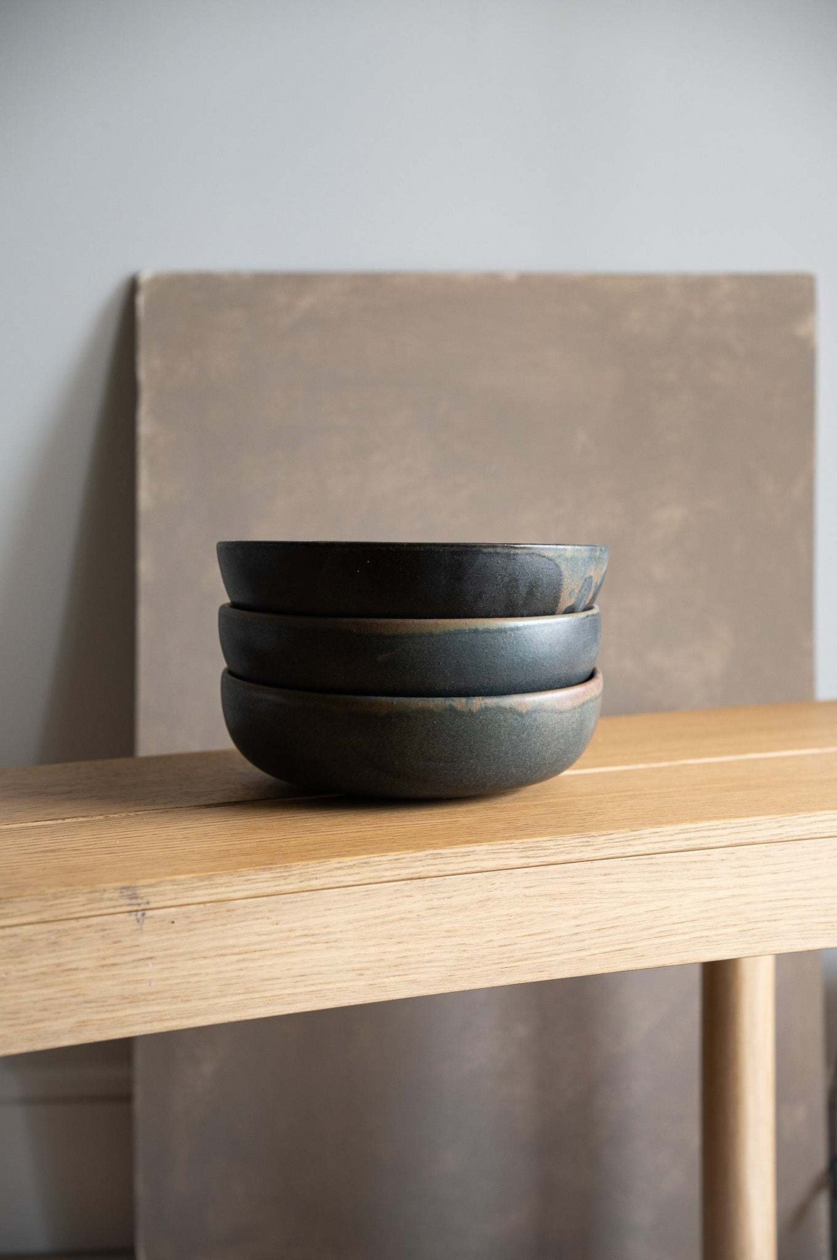 Stoneware pasta bowl set in charcoal gray matte glaze, with gently curved low-profile forms and subtle handmade color variations.