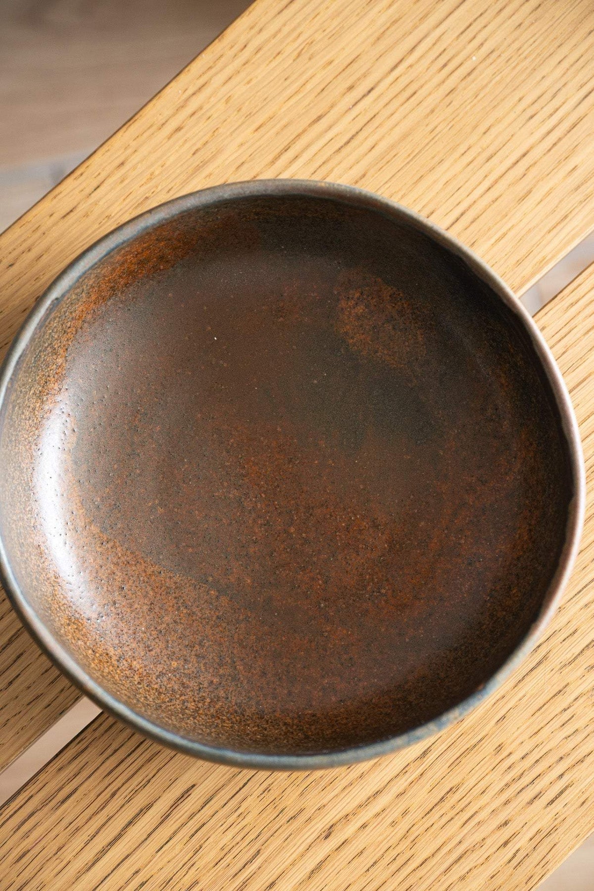 Rust stoneware pasta bowl with a round, low profile and dark brown matte glaze flecked with warm orange speckles.