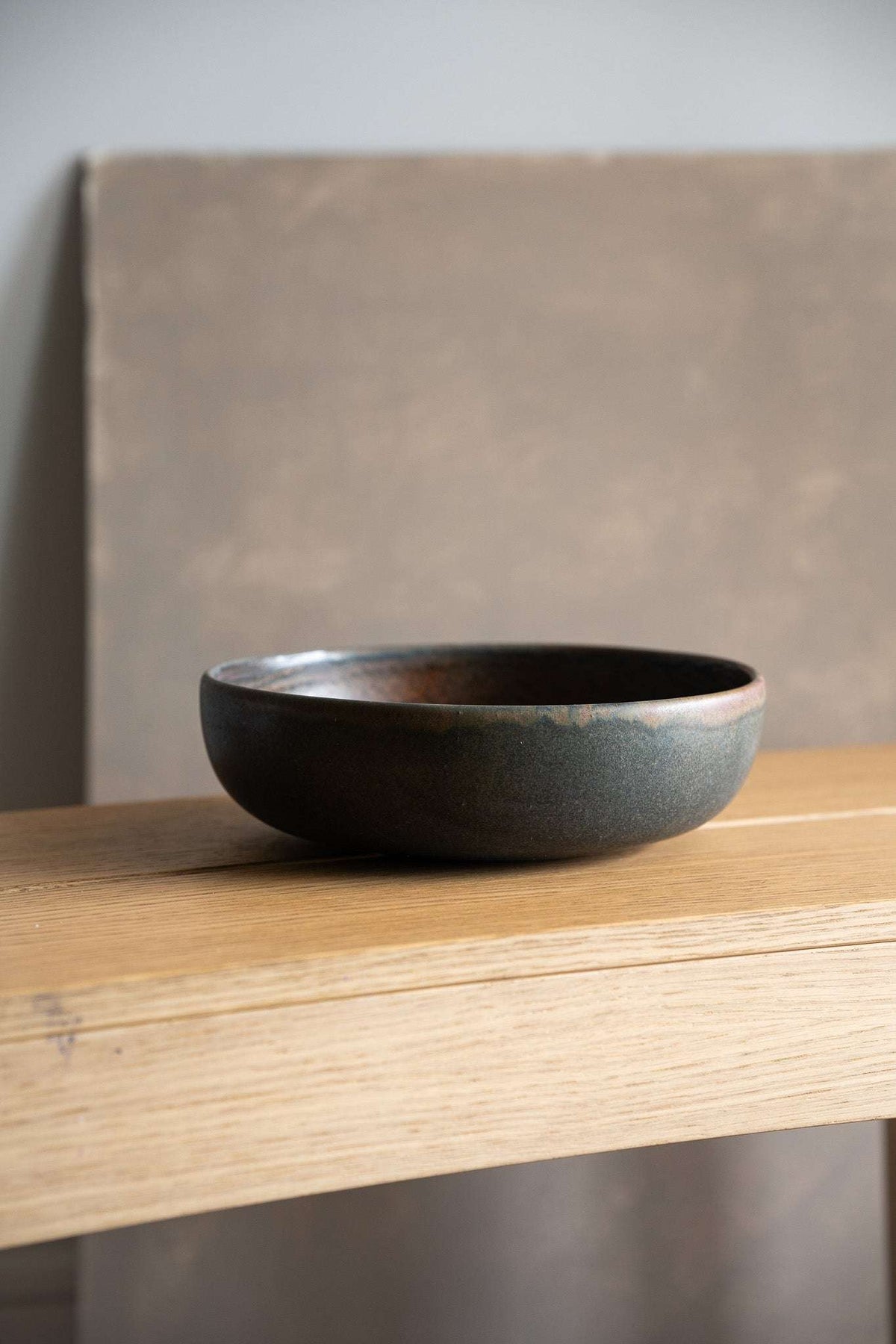Stoneware pasta bowl in dark charcoal stoneware with a smooth matte glaze, low rounded shape and subtle rust rim.