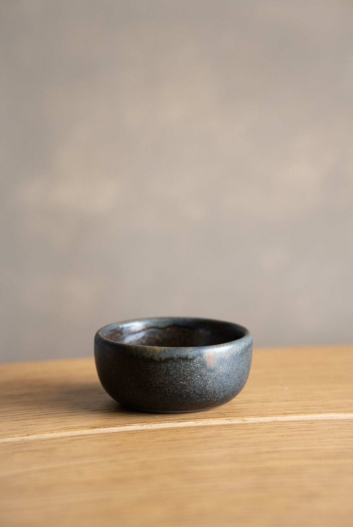 Rust Stoneware Pinch Bowl with a rounded shape, deep charcoal glaze, and subtle blue-gray speckling on the surface.