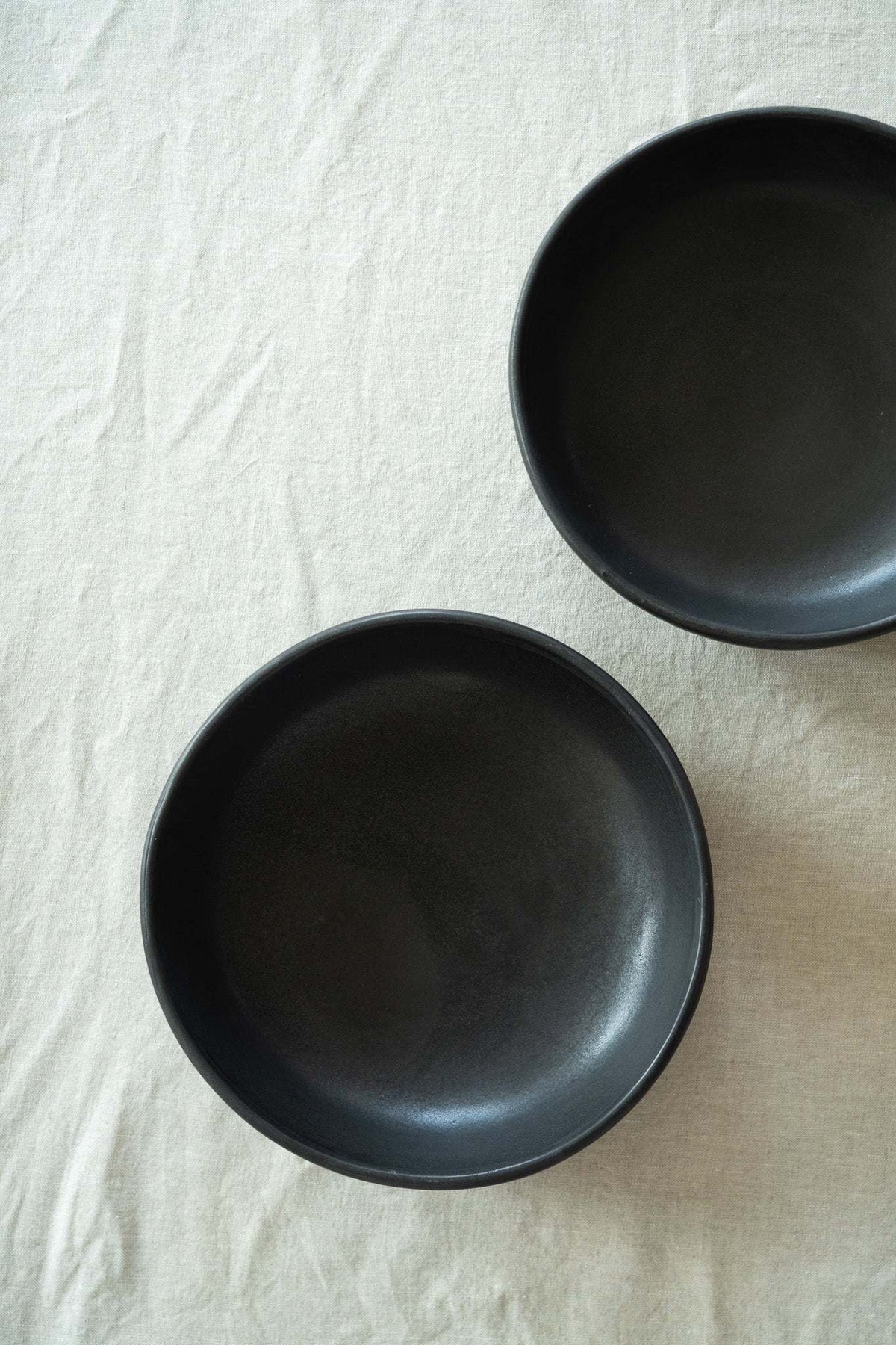 Black matte stoneware pasta bowl with a smooth finish, rounded rim, and shallow, wide profile.