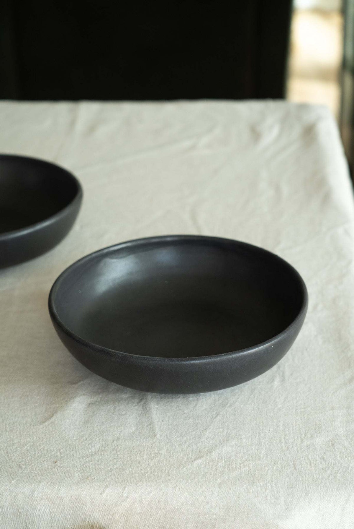 Black stoneware pasta bowl with a smooth matte finish, gently curved low-profile shape, and subtly irregular rim.
